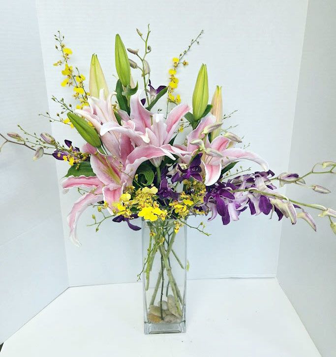 Pink lilies and purple orchids in a tall glass vase