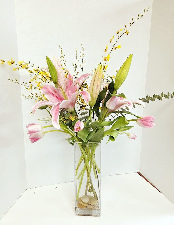 Pink lilies in a tall glass vase with yellow branching accents