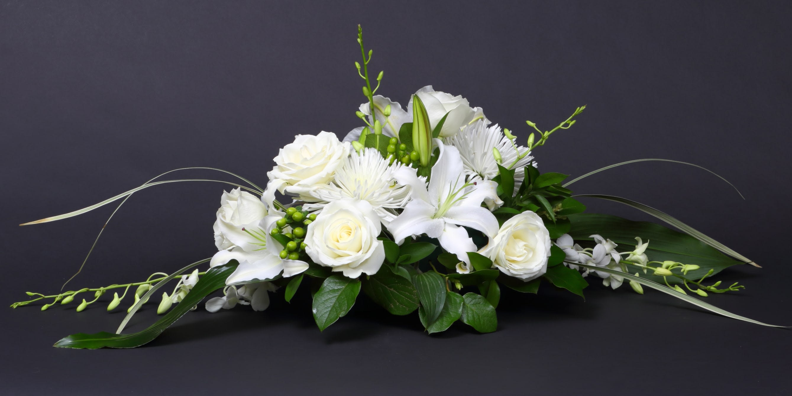 White floral centerpiece with roses and lilies on a dark background
