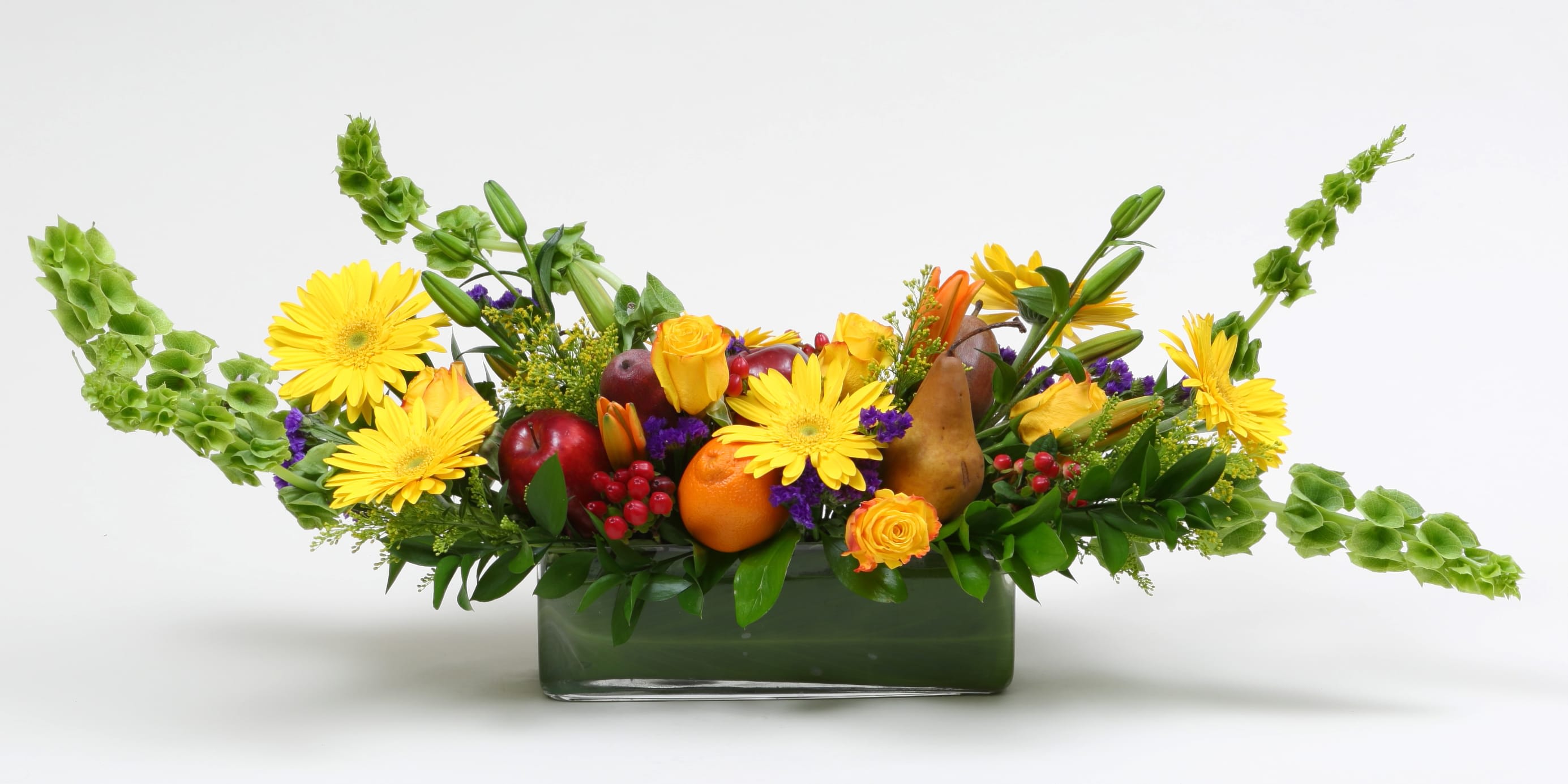Yellow daisies and fruit arranged in a rectangular glass vase