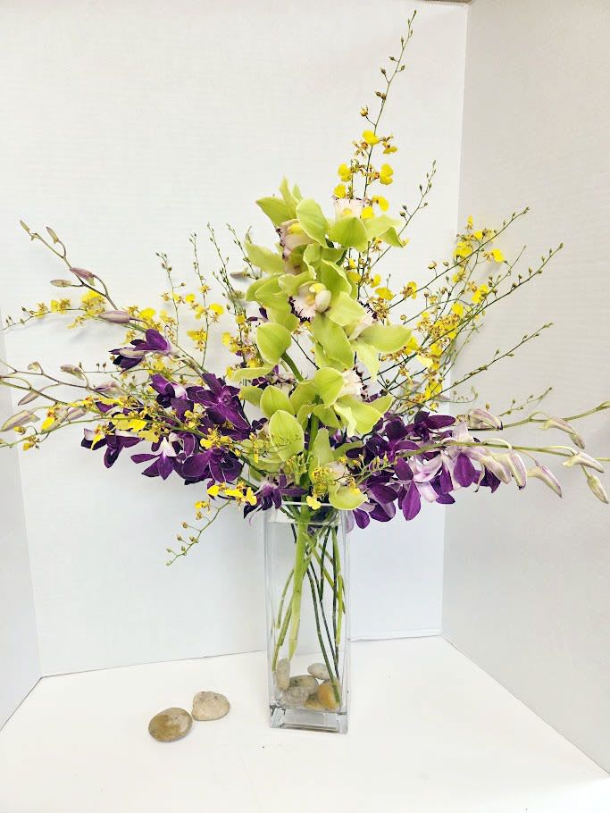 Tall orchid arrangement in a clear glass vase with yellow and purple blooms