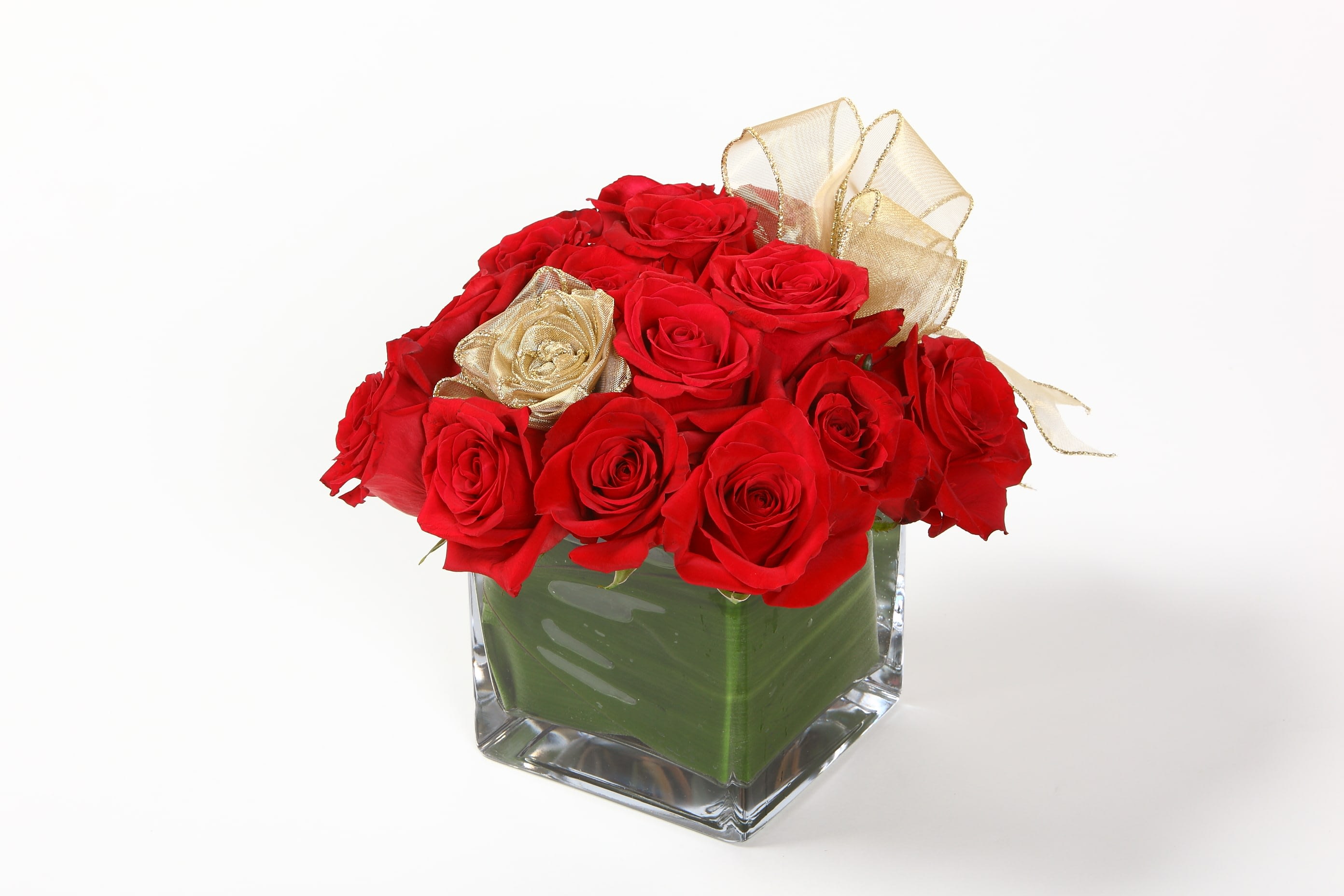 Red roses arranged in a clear square vase with gold ribbon accents