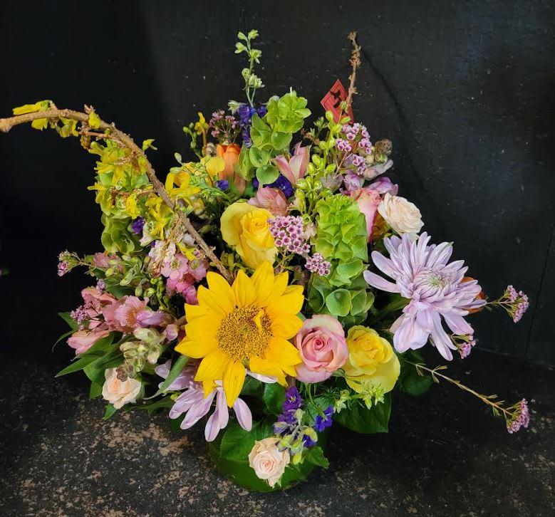Colorful mixed flower arrangement with sunflowers, roses, and purple daisies