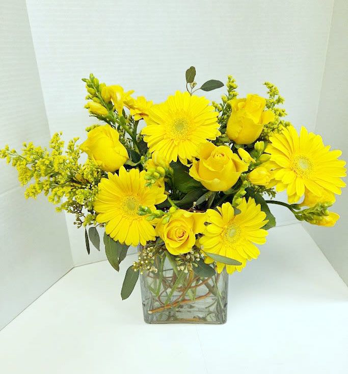 Yellow roses and gerbera daisies in a square glass vase