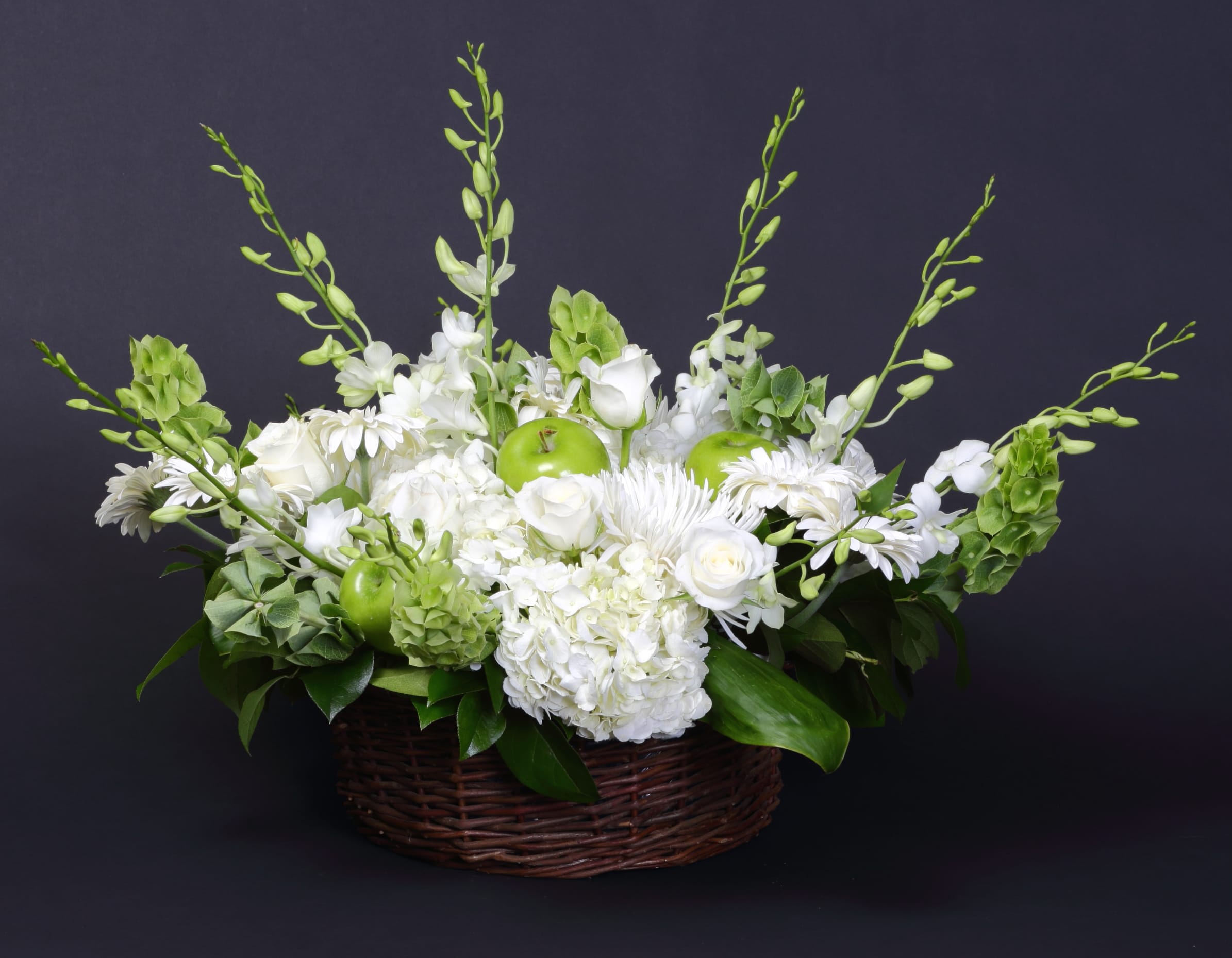 White floral arrangement in a wicker basket with green apples