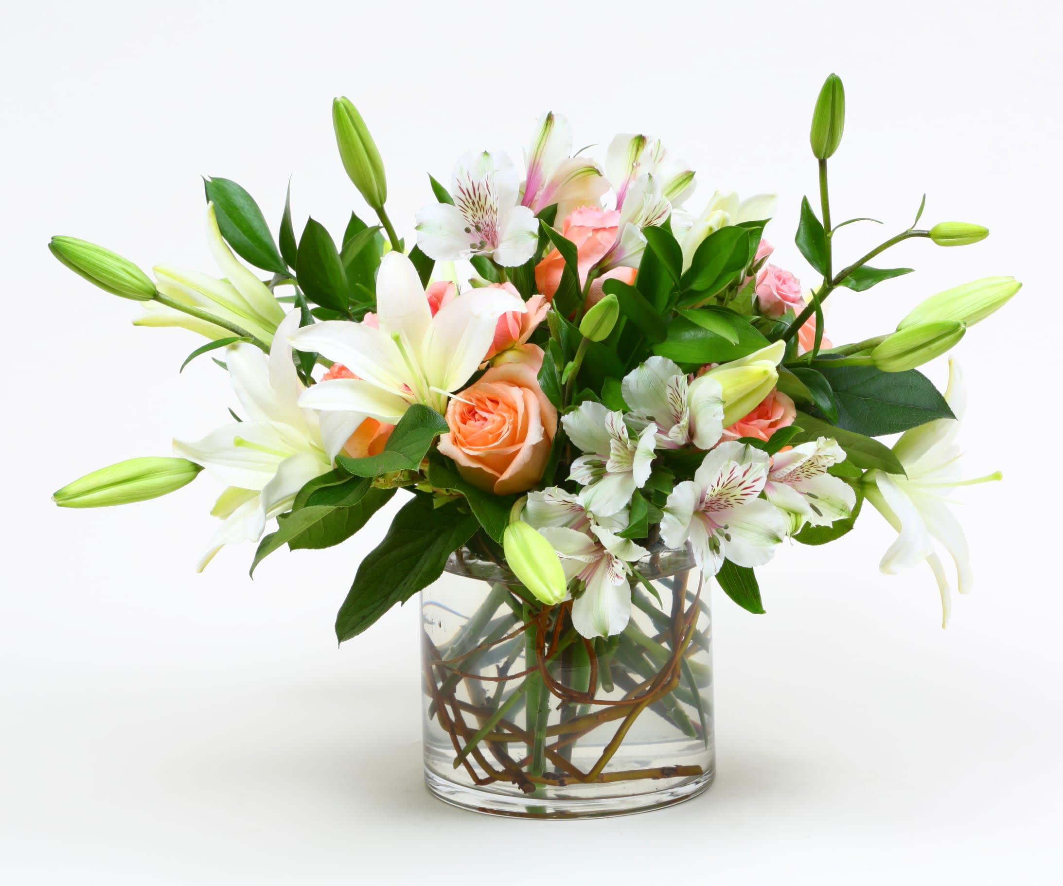 Bouquet of white lilies, peach roses, and white alstroemeria in a glass vase