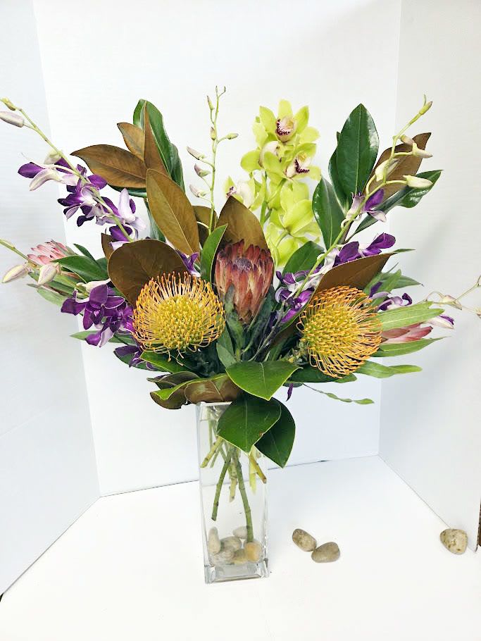 Tropical bouquet with orchids and protea in a clear glass vase
