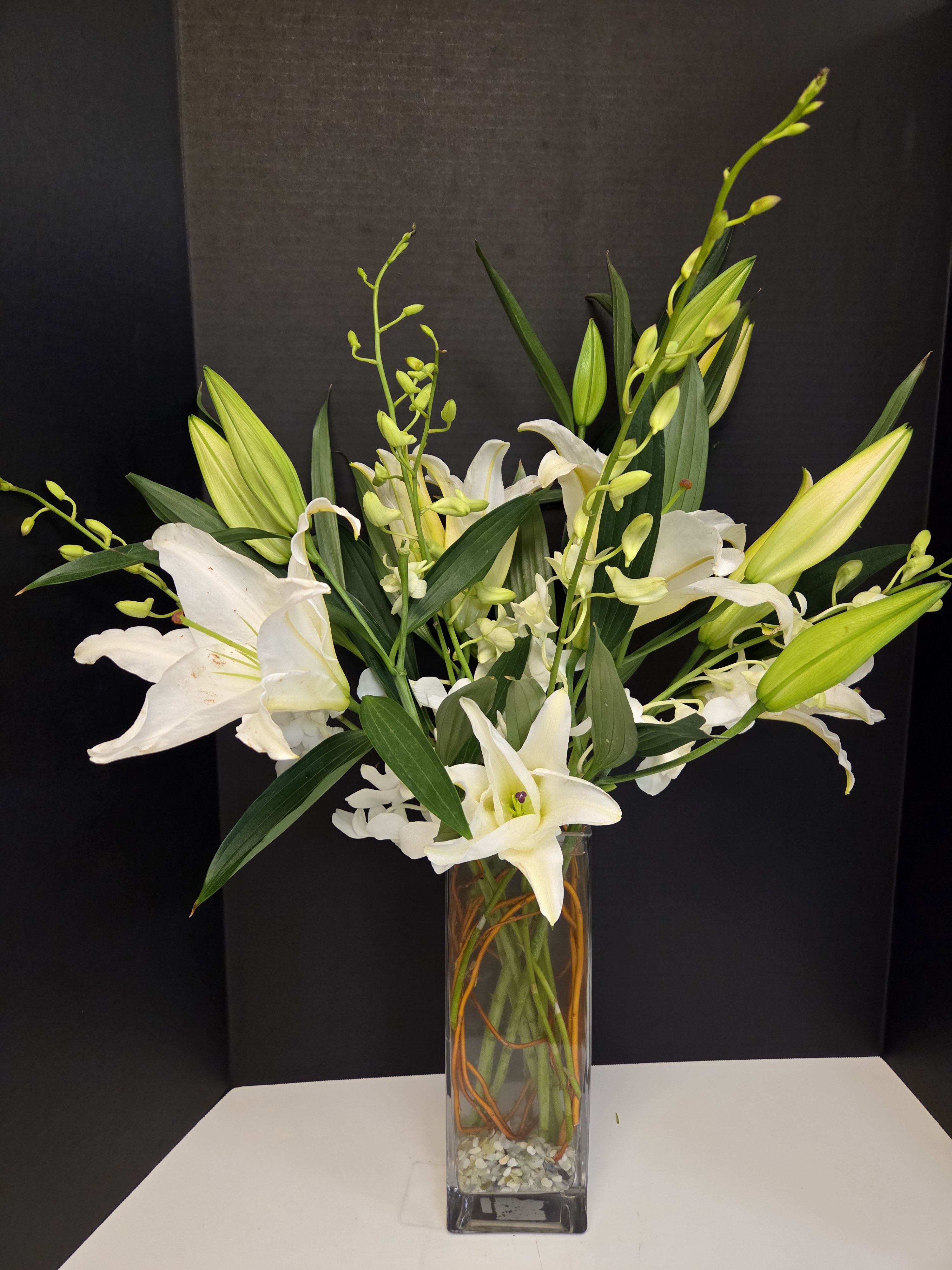White lilies and orchid stems in a tall glass vase