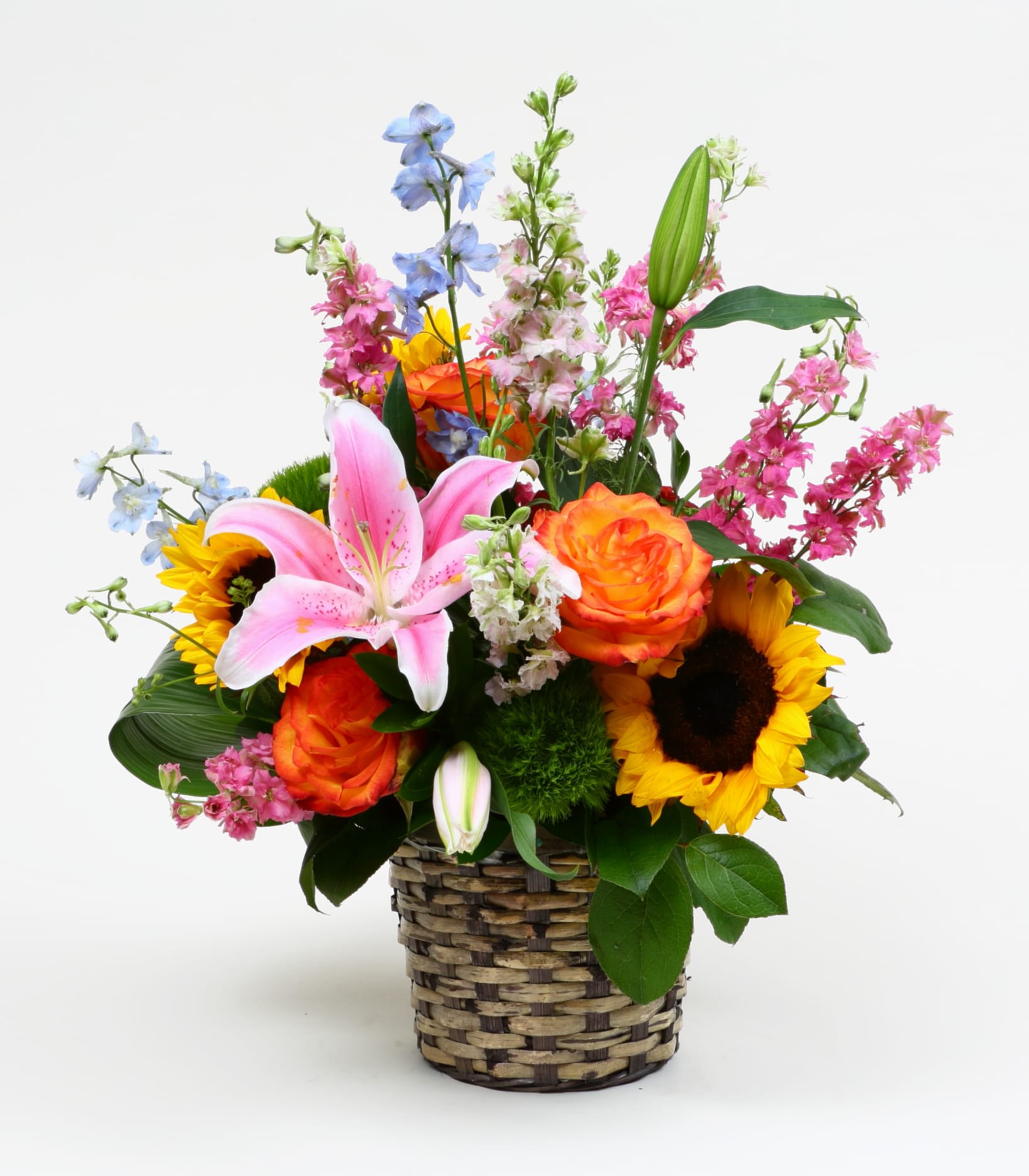 Mixed bouquet in a woven basket with lilies, roses, and sunflowers