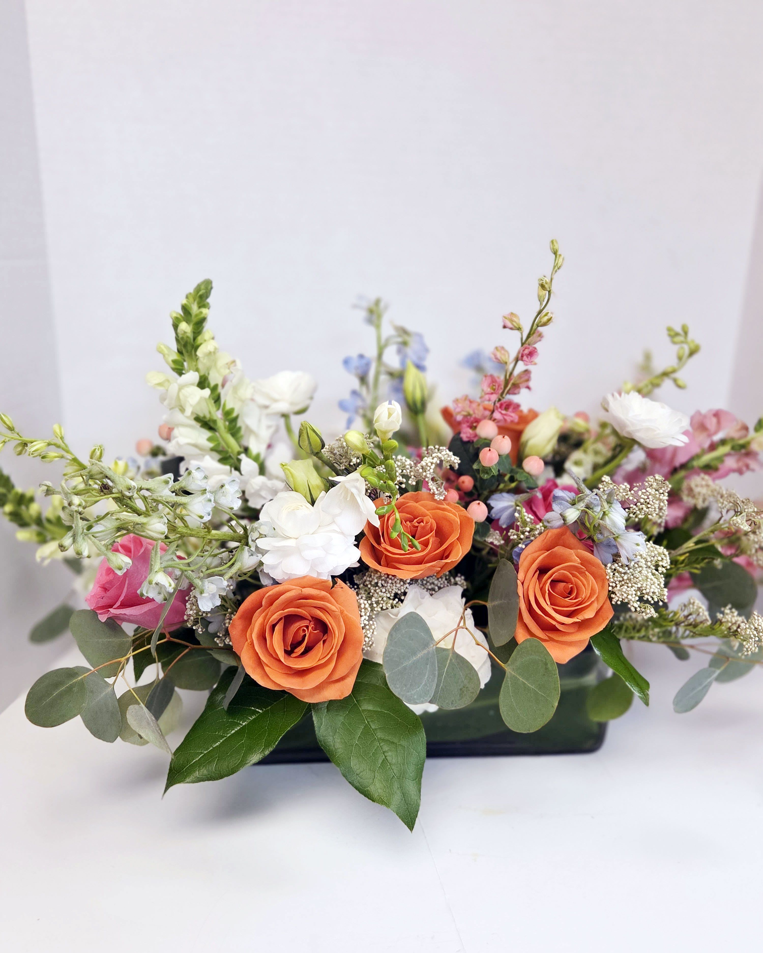 Low floral arrangement with orange and white roses in a black container