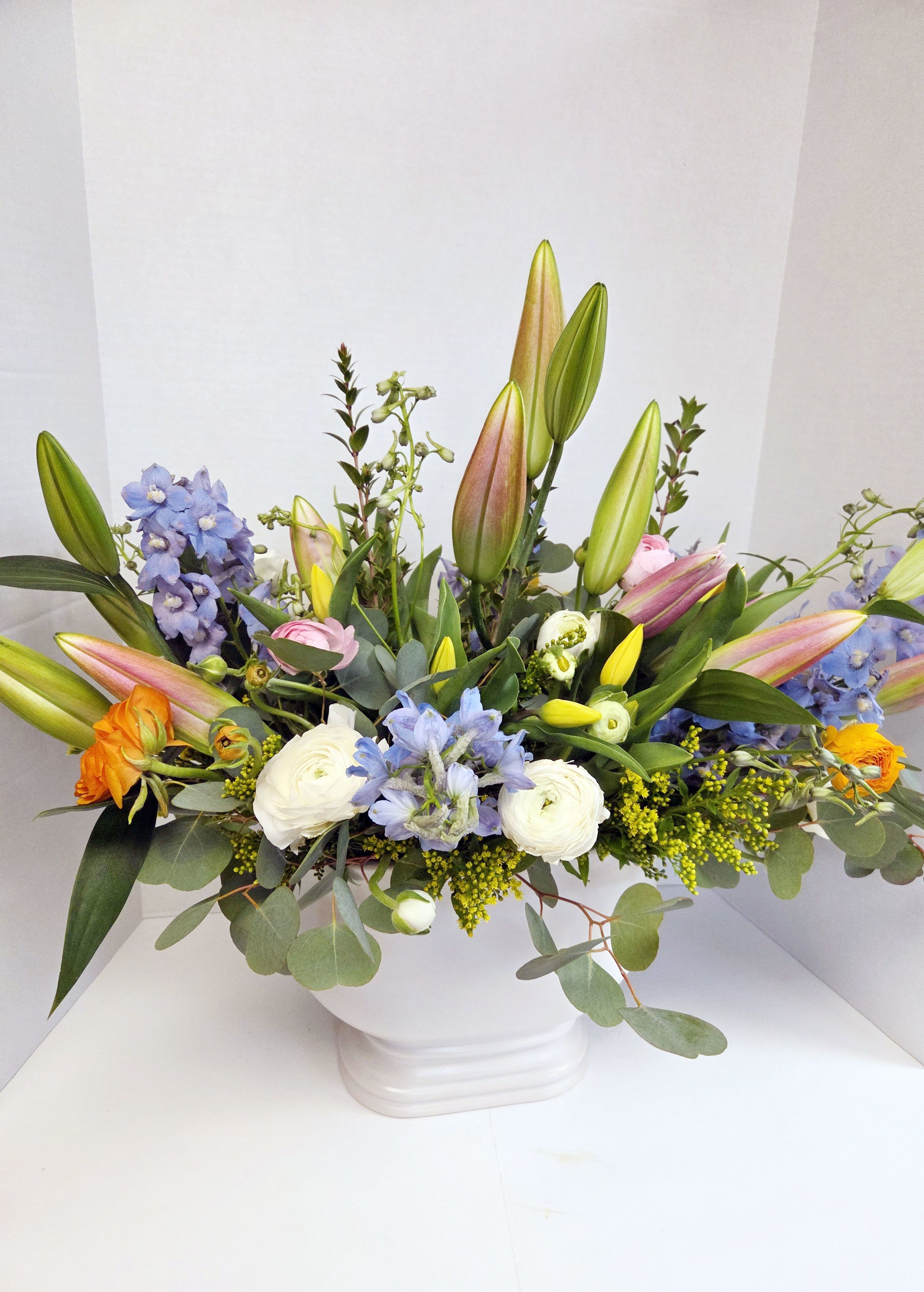 Mixed bouquet with lilies, blue flowers, and white blooms in a white vase