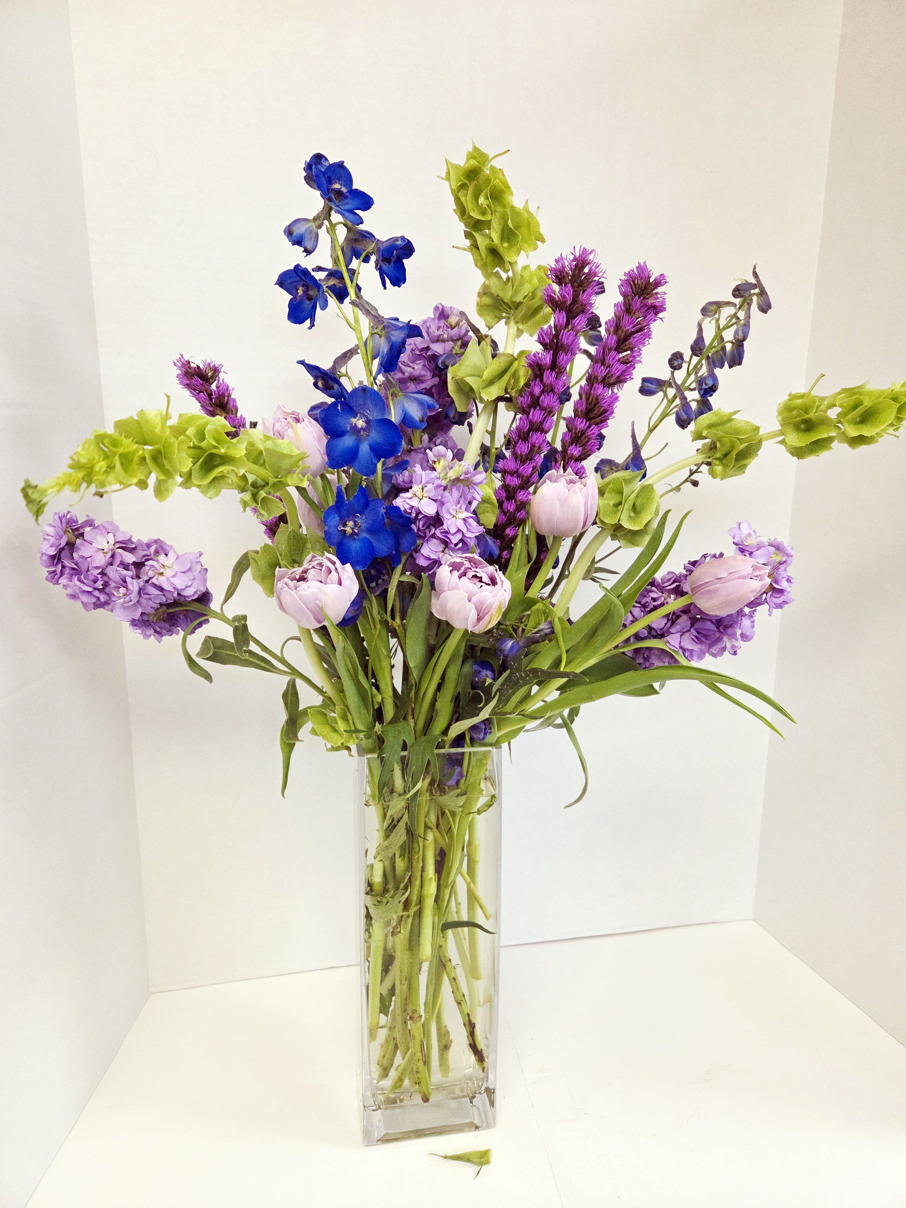 Tall vase arrangement with blue, purple, and pale pink flowers