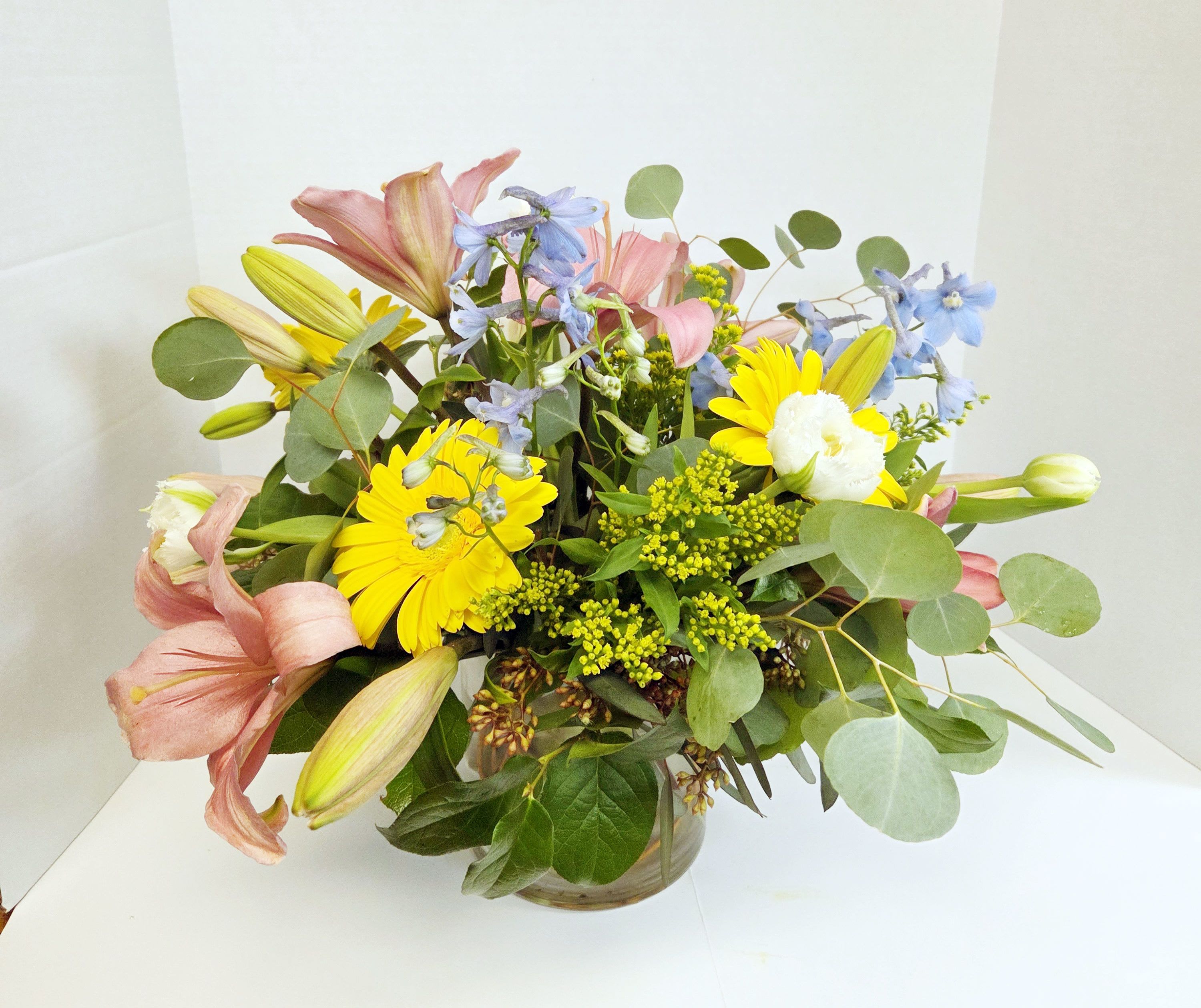 Mixed bouquet of lilies, daisies, and blue flowers in a glass vase