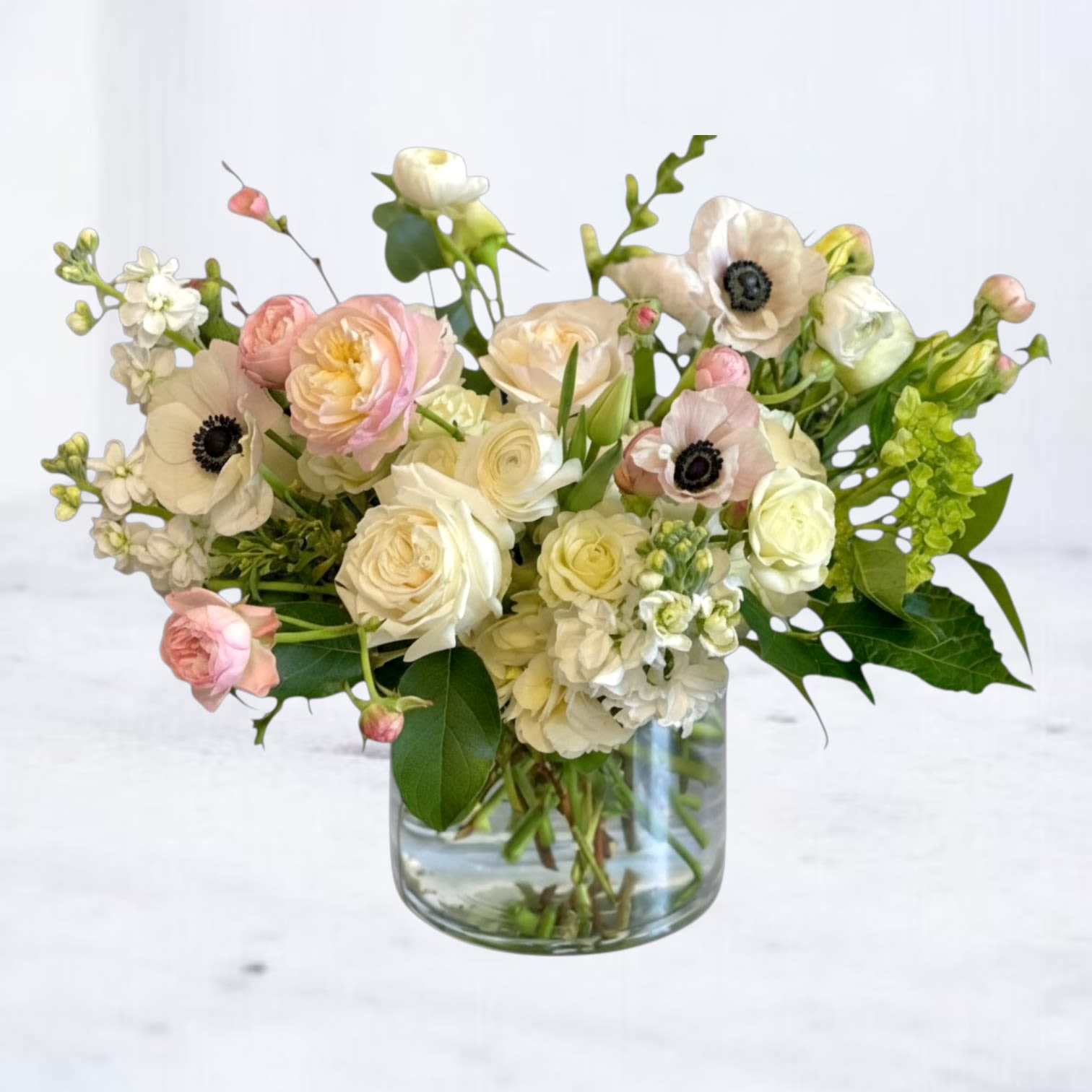 Petaline - Petaline is a soft, garden-inspired floral arrangement designed with delicate texture, airy movement, and a refined, neutral palette. Featuring blush and ivory roses, ranunculus, anemones, and seasonal accent blooms, this arrangement is layered with fresh greenery to create a naturally flowing, organic composition.  Designed in a clear glass vase, Petaline blends soft pastel tones with fresh greens for a look that feels both romantic and understated. The airy structure and layered textures give this arrangement a modern, editorial feel, offering a sophisticated alternative to traditional compact bouquets.  Perfect for sympathy flowers, anniversaries, new baby celebrations, thank-you gifts, or simply bringing a sense of calm beauty into the home, this blush and white floral arrangement delivers a timeless, elevated design.  Same-day flower delivery is available in Magnolia, TX, The Woodlands, Montgomery, Conroe, Spring, Tomball, and surrounding North Houston areas.  Due to seasonal availability, some blooms may be replaced with similar varieties of equal or greater value to maintain the design’s look and integrity. Your arrangement will always reflect the same color palette, style, and premium quality.