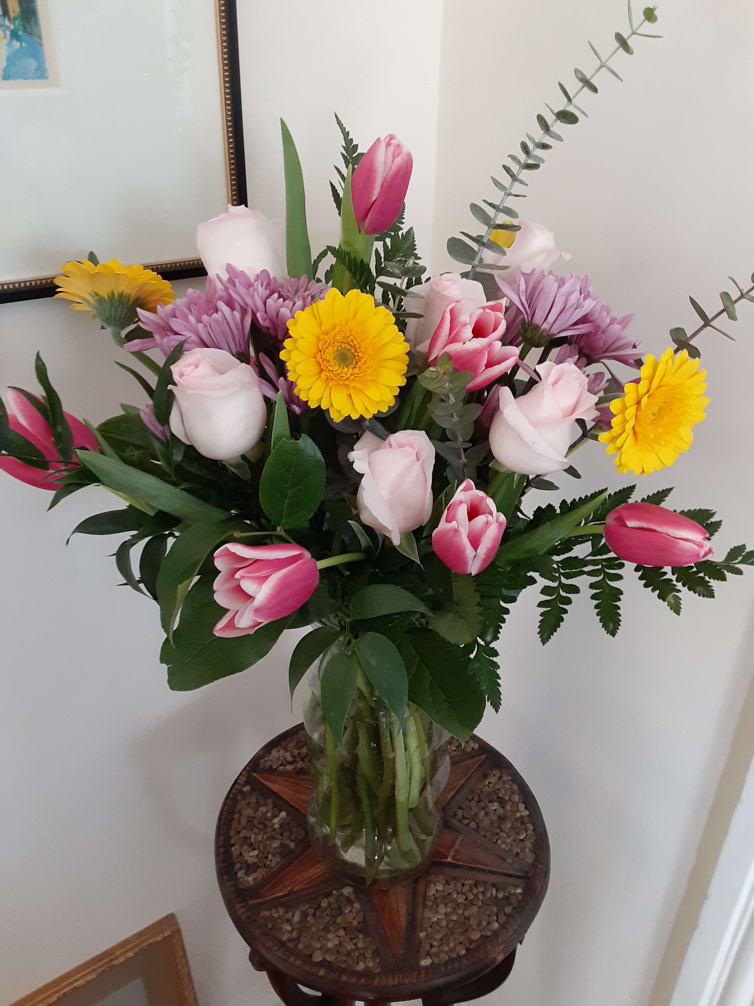 Mixed bouquet of pink tulips, pale roses, and yellow daisies in a glass vase