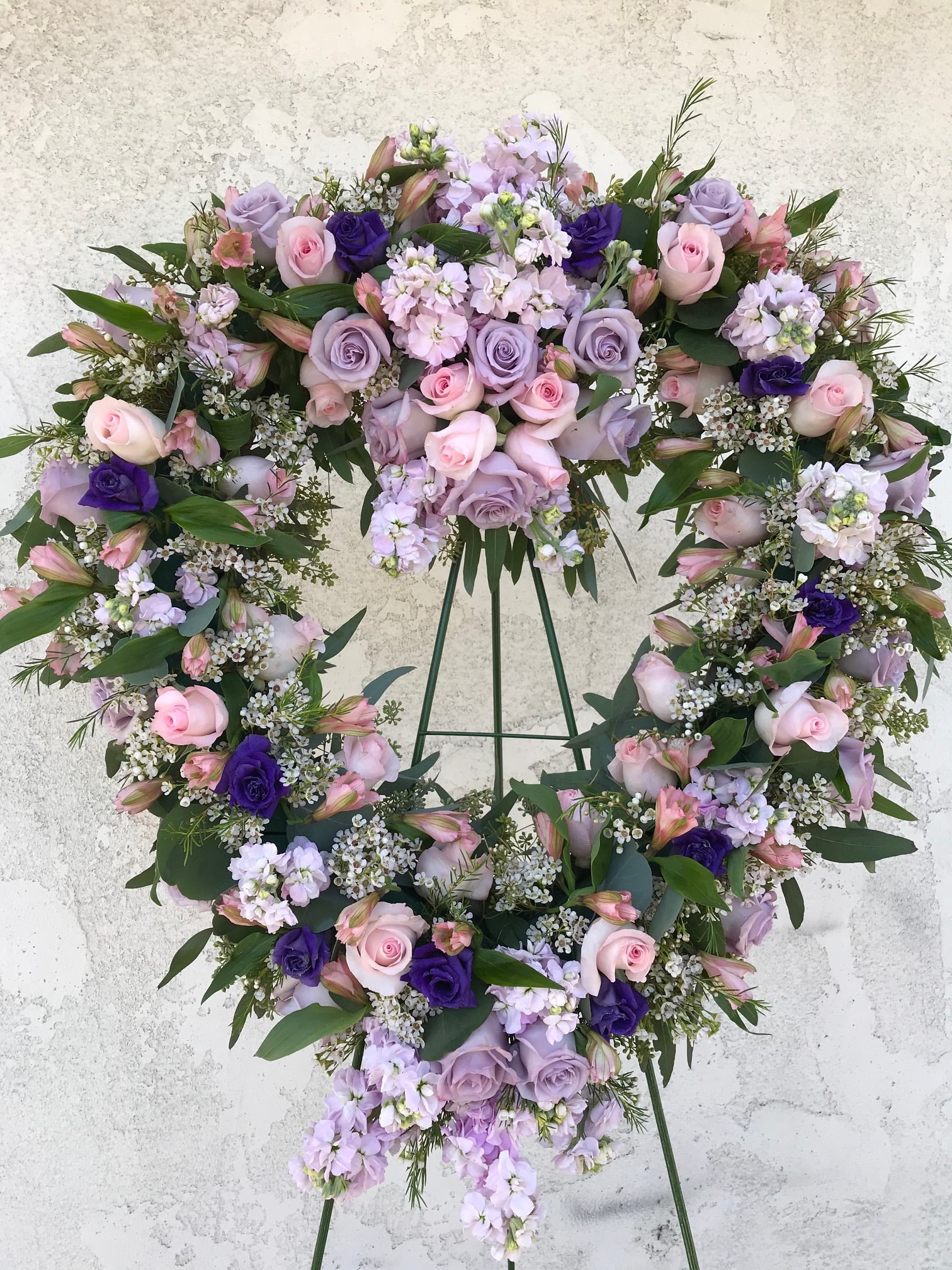 Heart-shaped floral wreath with pink and lavender roses on a stand