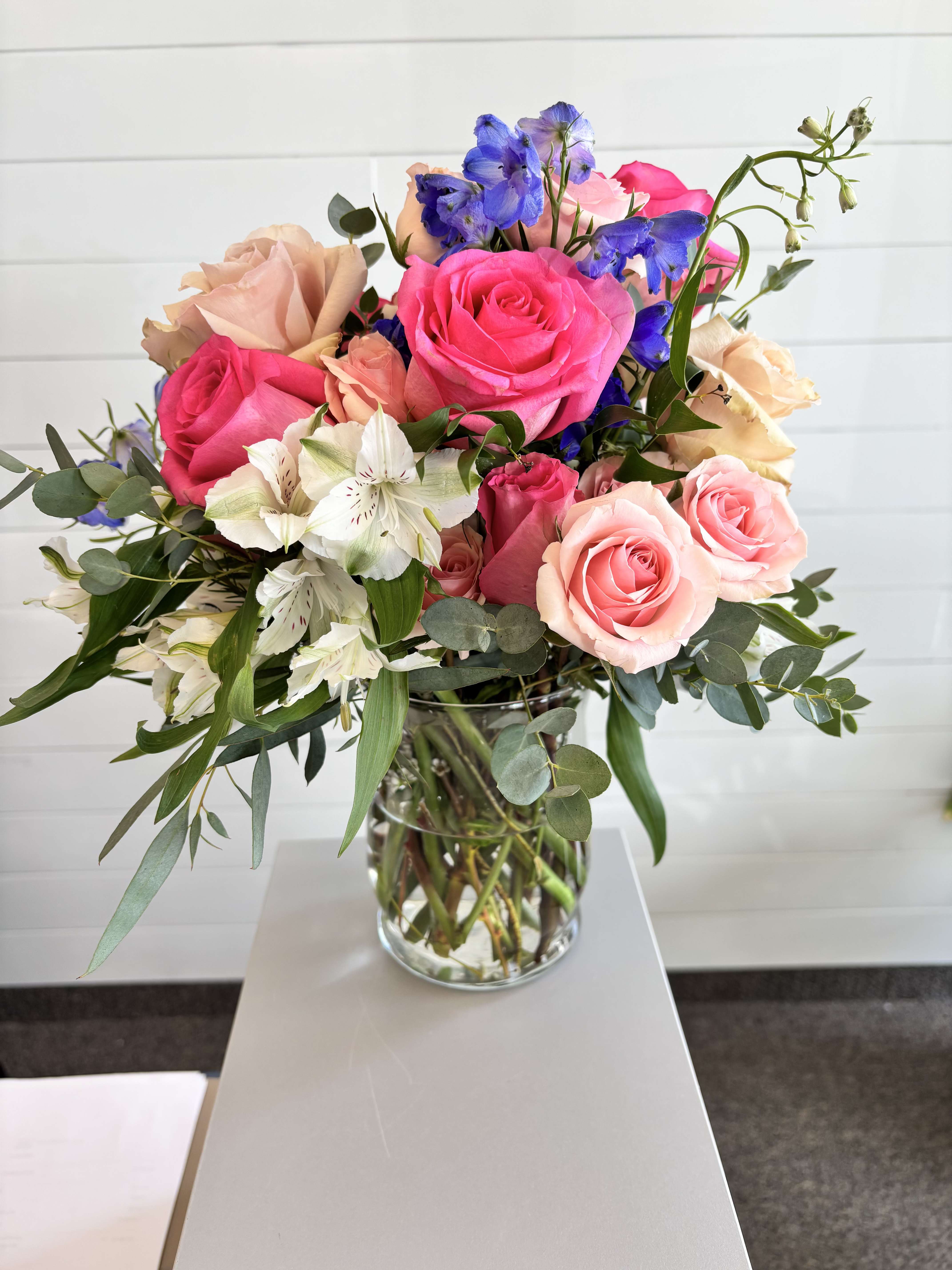 The Donna (Vase Arrangement) - A lush, garden-style arrangement designed to feel soft, vibrant, and full of life. Featuring a mix of premium blooms in shades of pink, peach, and soft white, accented with subtle pops of color and fresh greenery, all arranged in a clear glass vase.  Includes:  Roses in assorted shades of pink and peach Complementary seasonal blooms Fresh greenery Clear glass vase  Each arrangement is hand-designed, with slight variations based on the freshest flowers available.
