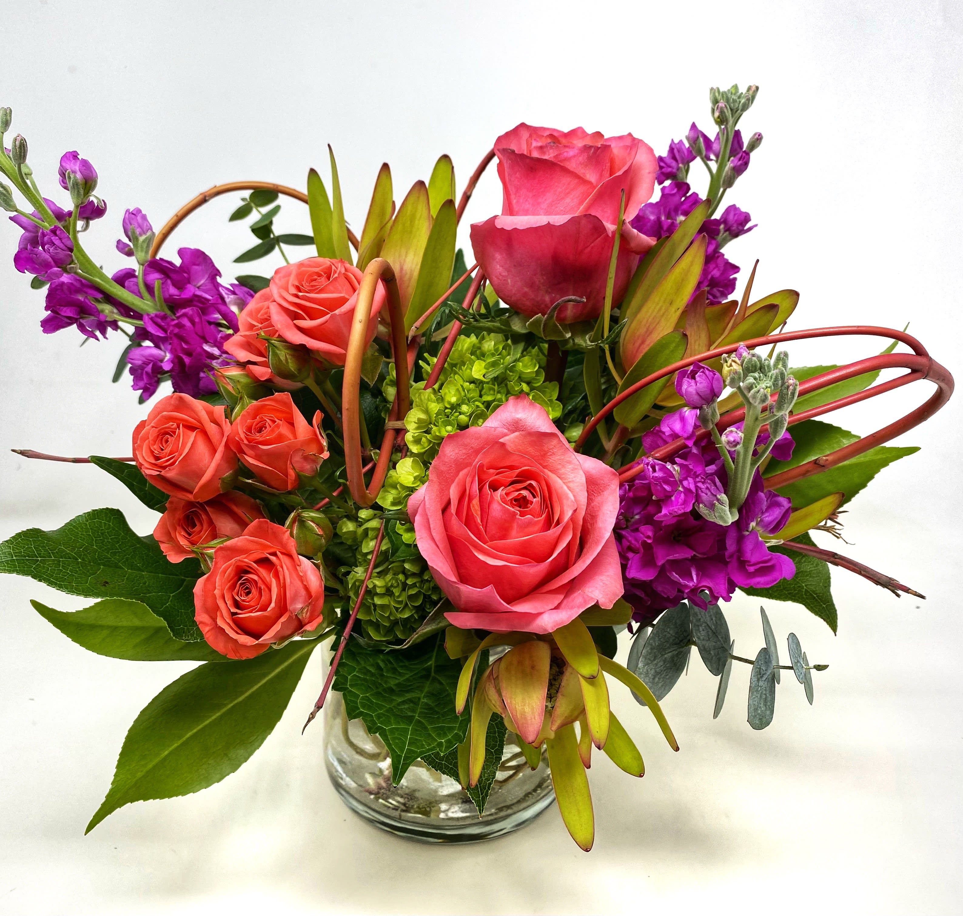 Pink and coral roses with purple flowers in a glass vase
