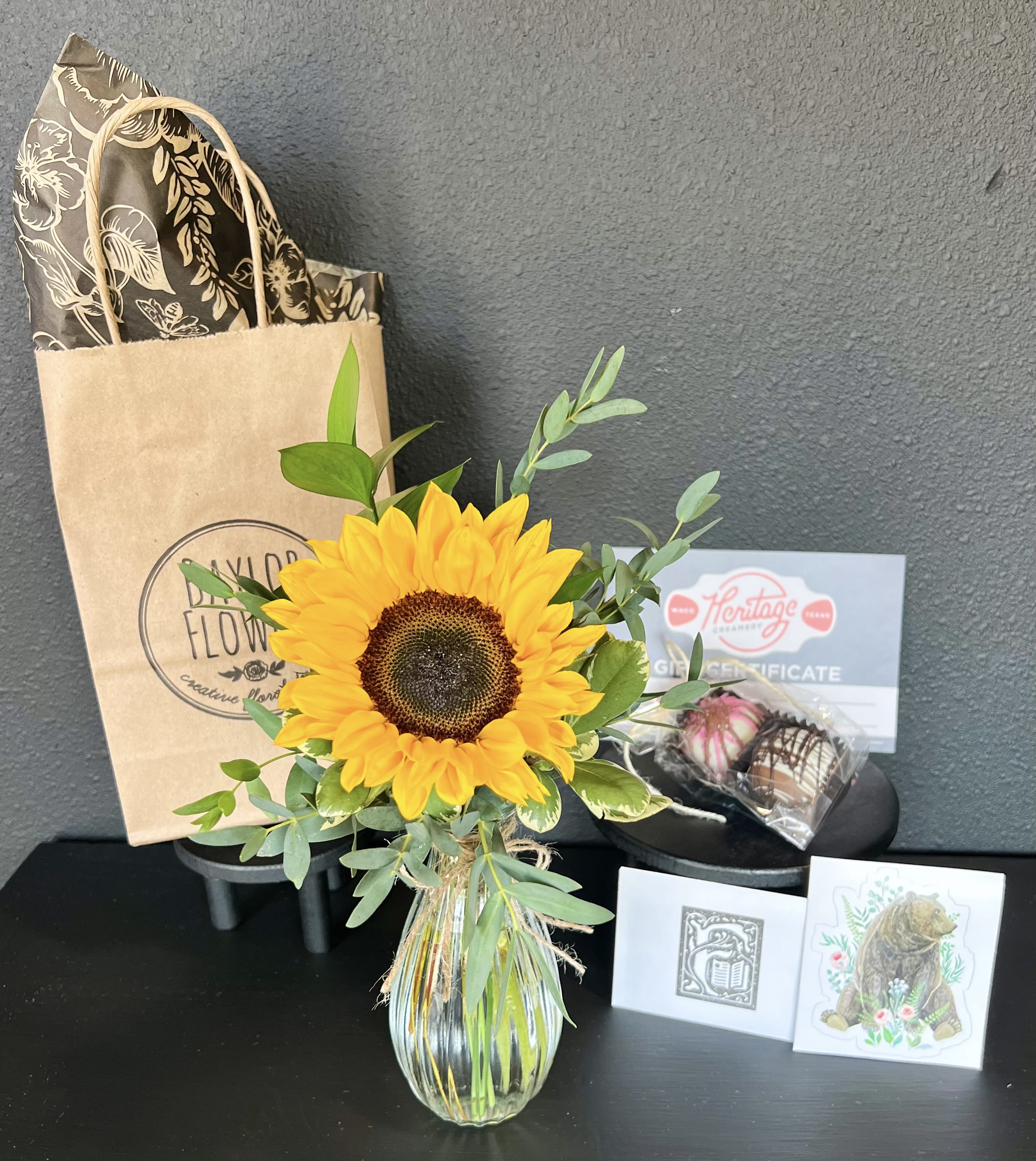 Sunflower arrangement in a glass vase with a gift bag and chocolates