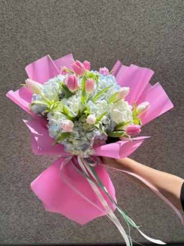 Tulips Wrapping Bouquet  - Pale blue hydrangeas paired with pink and white tulips create a soft, romantic tulips wrapping bouquet perfect for a birthday bouquet or an everyday celebration. The cool blue and warm pink tones read as fresh and affectionate, making this arrangement an ideal way to say "thinking of you" or "congratulations" to someone special-she'll feel gently celebrated the moment it arrives.  Hand-tied into a rounded shape, the arrangement is nestled in bright pink wrapping paper and finished with a trailing ribbon for a gift-ready presentation. The mix of lush hydrangea heads and graceful tulip stems gives appealing texture and a soft, fragrant presence that works well on tabletops or as a bedside surprise. Order now for delivery to mark an anniversary, thank-you, or just-because moment; simple care-fresh water and a cool spot-will keep the blooms looking lovely for days.