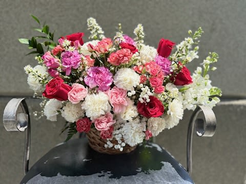 color full Basket  - A lush, rounded basket overflowing with pink, red, and white blooms makes a joyful statement for birthdays, anniversaries, or a thoughtful "thinking of you" surprise. This flower arrangement places roses and ruffled carnations front and center for a soft, layered texture while white stock spires lift the composition with an airy vertical accent-delivering a romantic yet cheerful look that will make the person you're thinking of feel truly celebrated.  Fresh roses, carnations, daisies, and stock are artfully arranged in a woven basket that adds a warm, rustic touch and keeps the display casual enough for everyday gifting. The palette of rosy pinks, vivid reds, and clean whites creates contrast and depth; the compact, full form reads elegant from every angle and fits well on a dining table, desk, or entry console.  Perfect for marking special moments or brightening someone's day, this arrangement arrives ready to display-basket included-and is sized to be a generous tabletop centerpiece without overwhelming a room. For longevity, refresh the water daily and trim stems slightly when rehydrating to help the blooms stay vibrant longer.