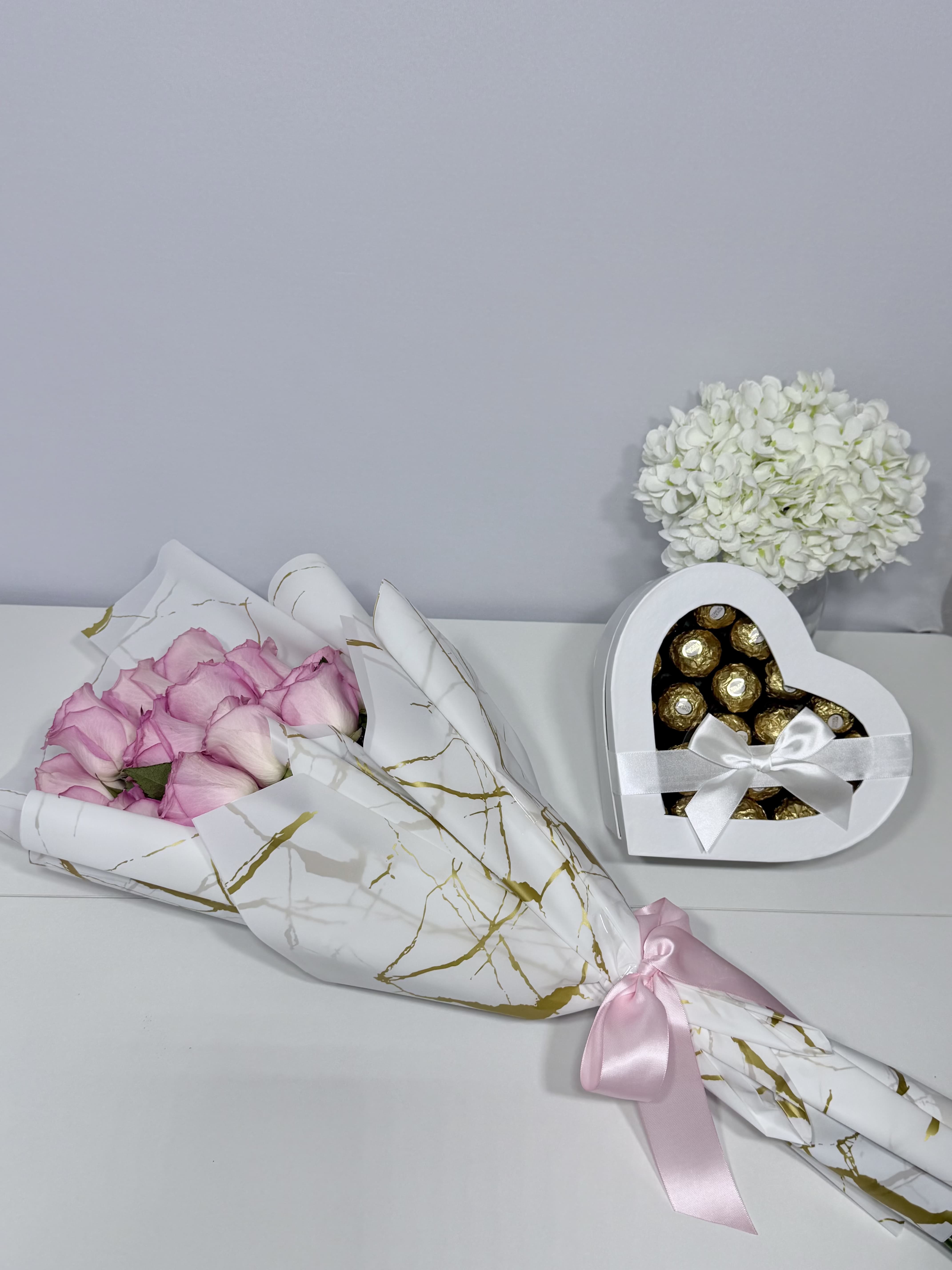 Golden Blush  - Delicate blush roses beautifully wrapped in elegant white and gold paper, paired with a heart-shaped chocolate box for sweet and memorable moments.