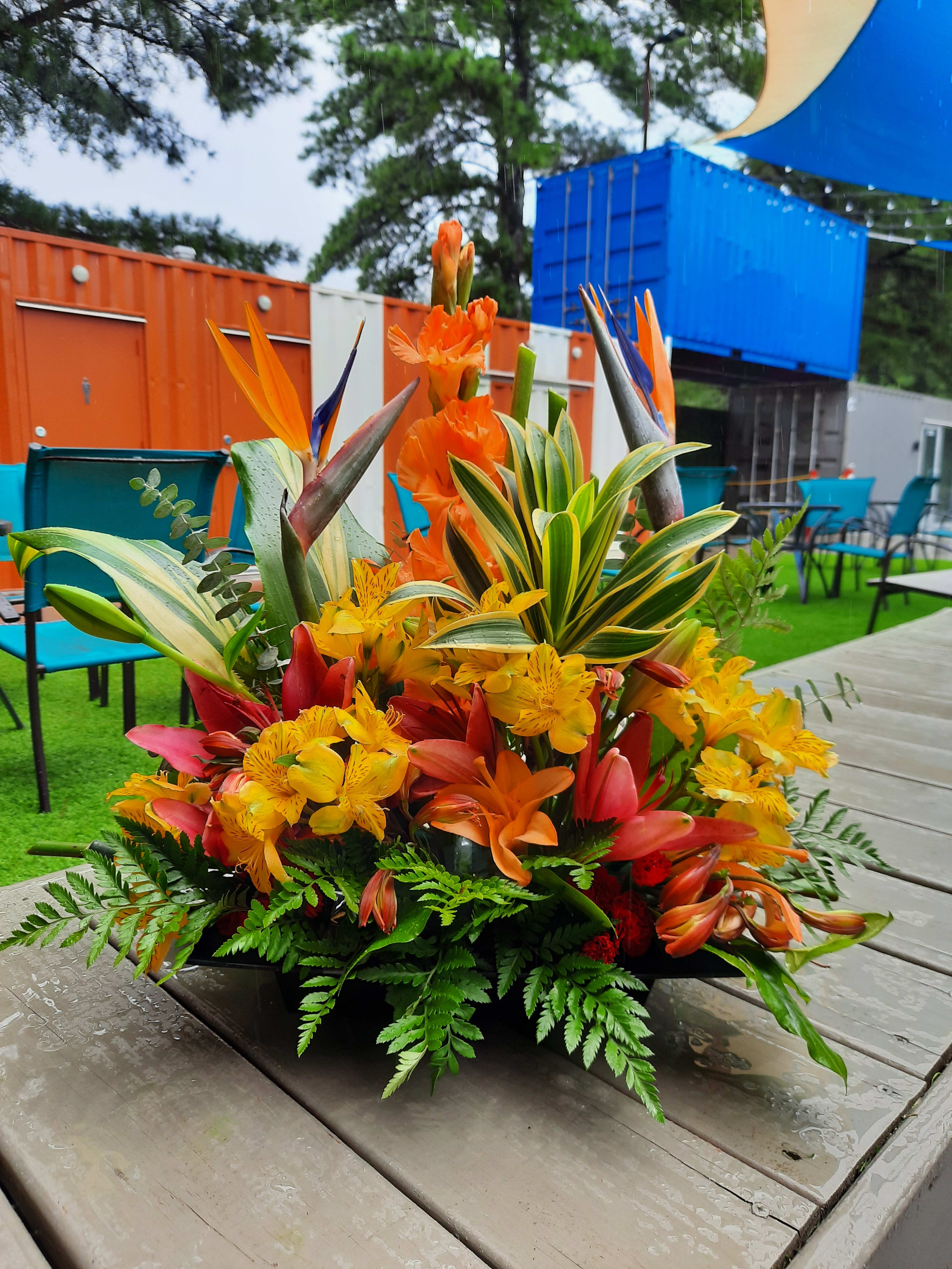Tropical floral arrangement with orange, yellow, and red blooms in a low container