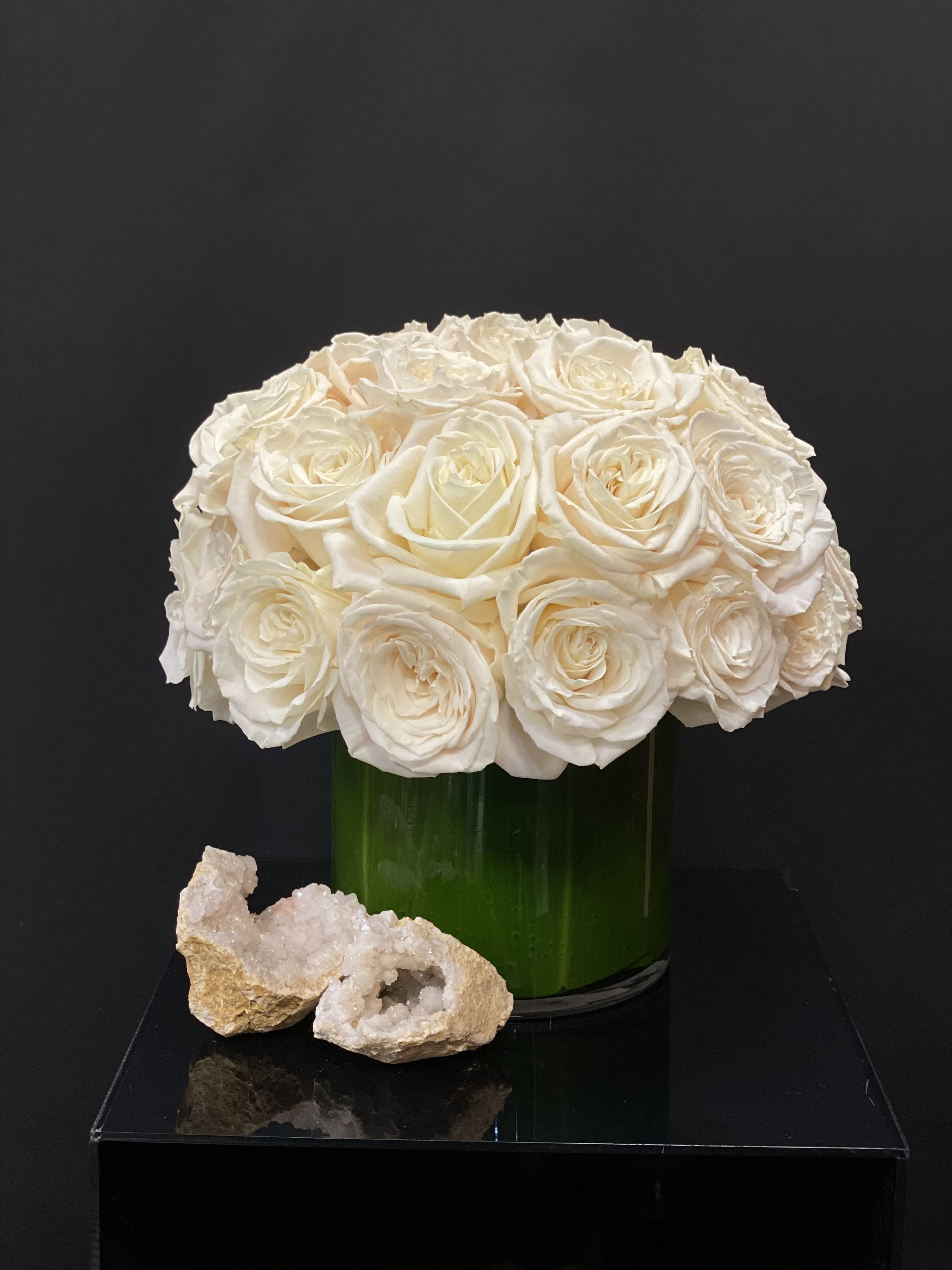 White rose bouquet in a green glass vase with two crystal rocks in front