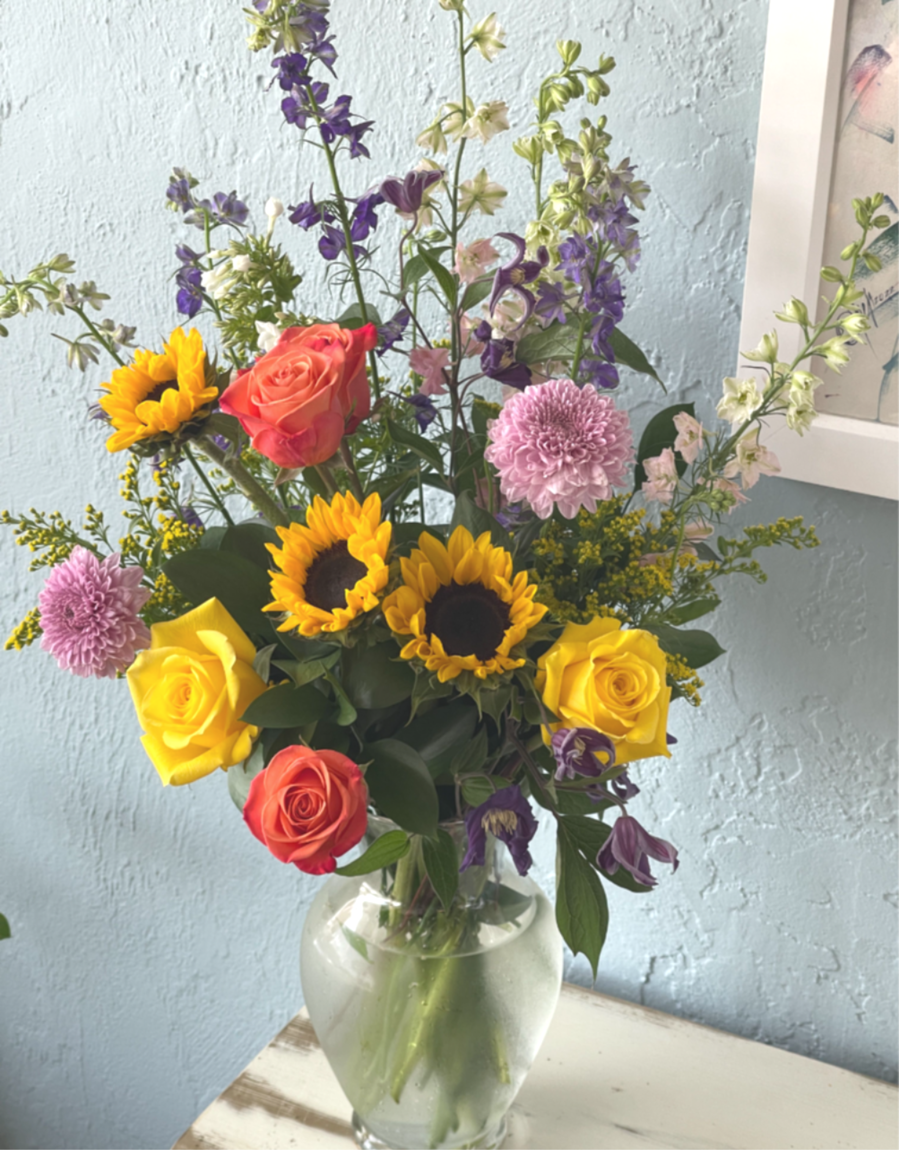 Mixed bouquet of sunflowers, roses, and purple flowers in a glass vase