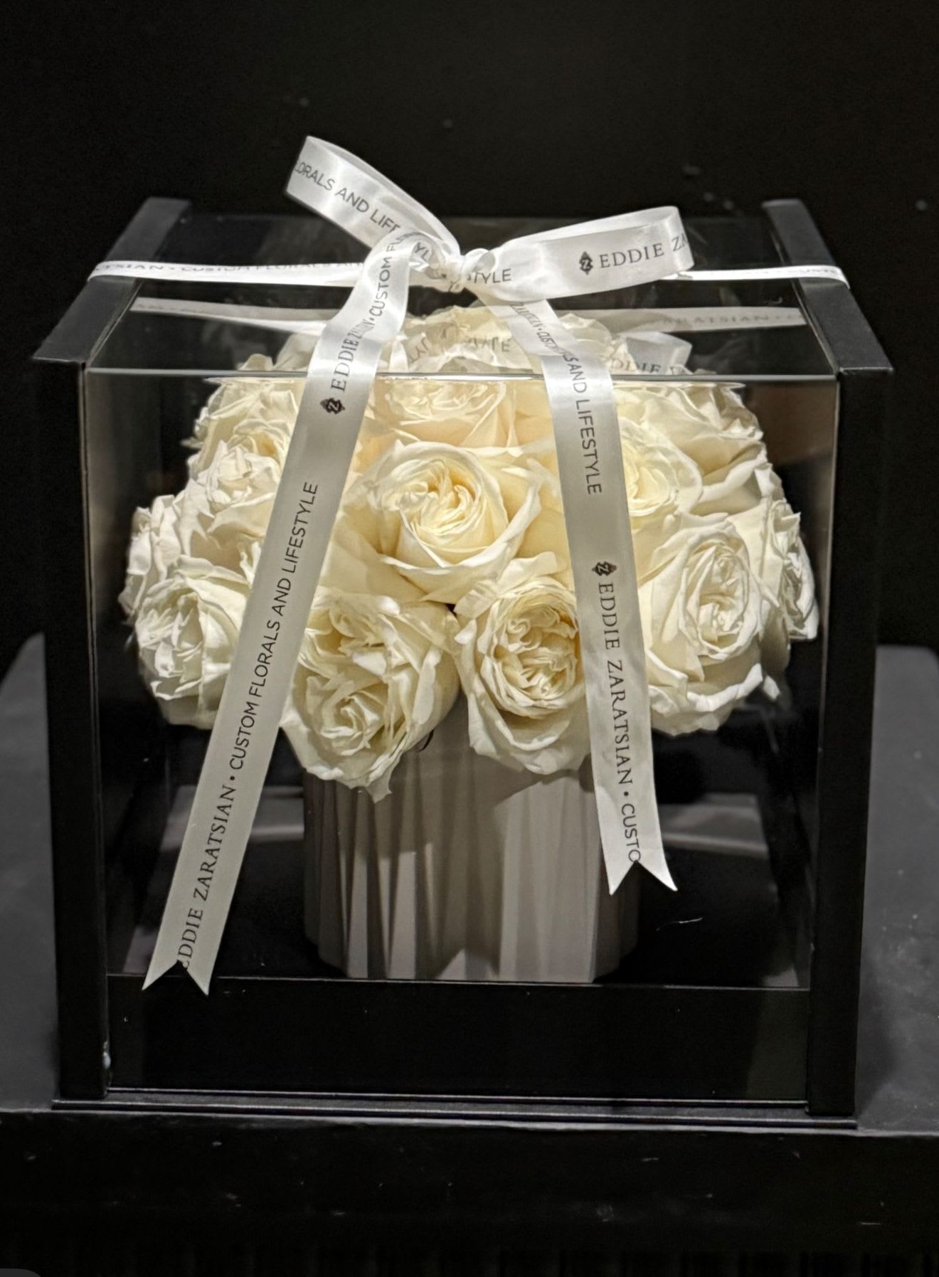 White roses arranged in a black gift box with a ribbon bow