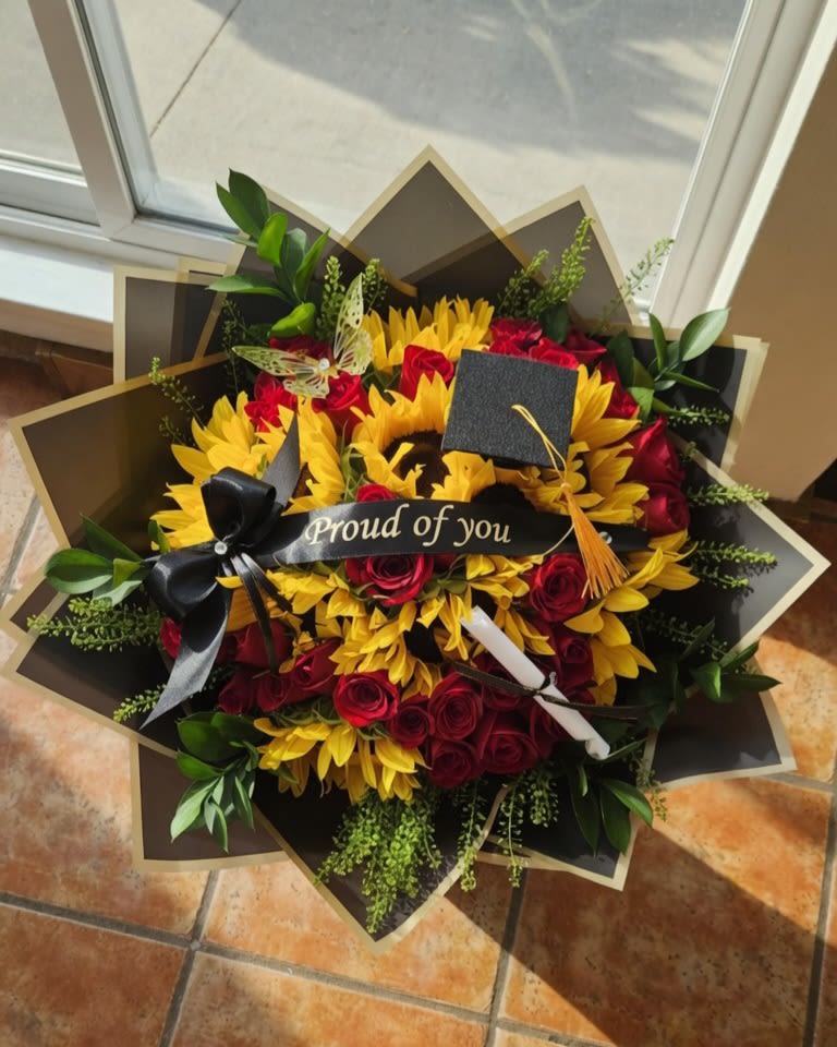 Ramo de Graduación_Girasoles y Rosas Rojas - Celebra este logro inolvidable con nuestro exclusivo ramo de flores para graduación. Diseñado para transmitir orgullo y admiración, este espectacular arreglo floral combina la vibrante energía de los girasoles grandes con la elegancia clásica de las rosas rojas, creando un contraste de color único y sofisticado. ​Cada detalle de este ramo ha sido cuidadosamente pensado para la ocasión: incluye una cinta elegante con la frase "Proud of you" (Orgulloso/a de ti), un minicapelo de graduación (birrete) con su borla dorada, un pequeño diploma decorativo y una delicada mariposa calada que simboliza el inicio de una nueva etapa. Todo esto envuelto en un sofisticado papel de diseño geométrico en tonos oscuros con bordes dorados que hace resaltar cada flor. ​Es el regalo de graduación perfecto para desearle el mayor de los éxitos a esa persona especial en su entrega de diplomas. ¡Haz tu pedido hoy y celebra su esfuerzo a lo grande!