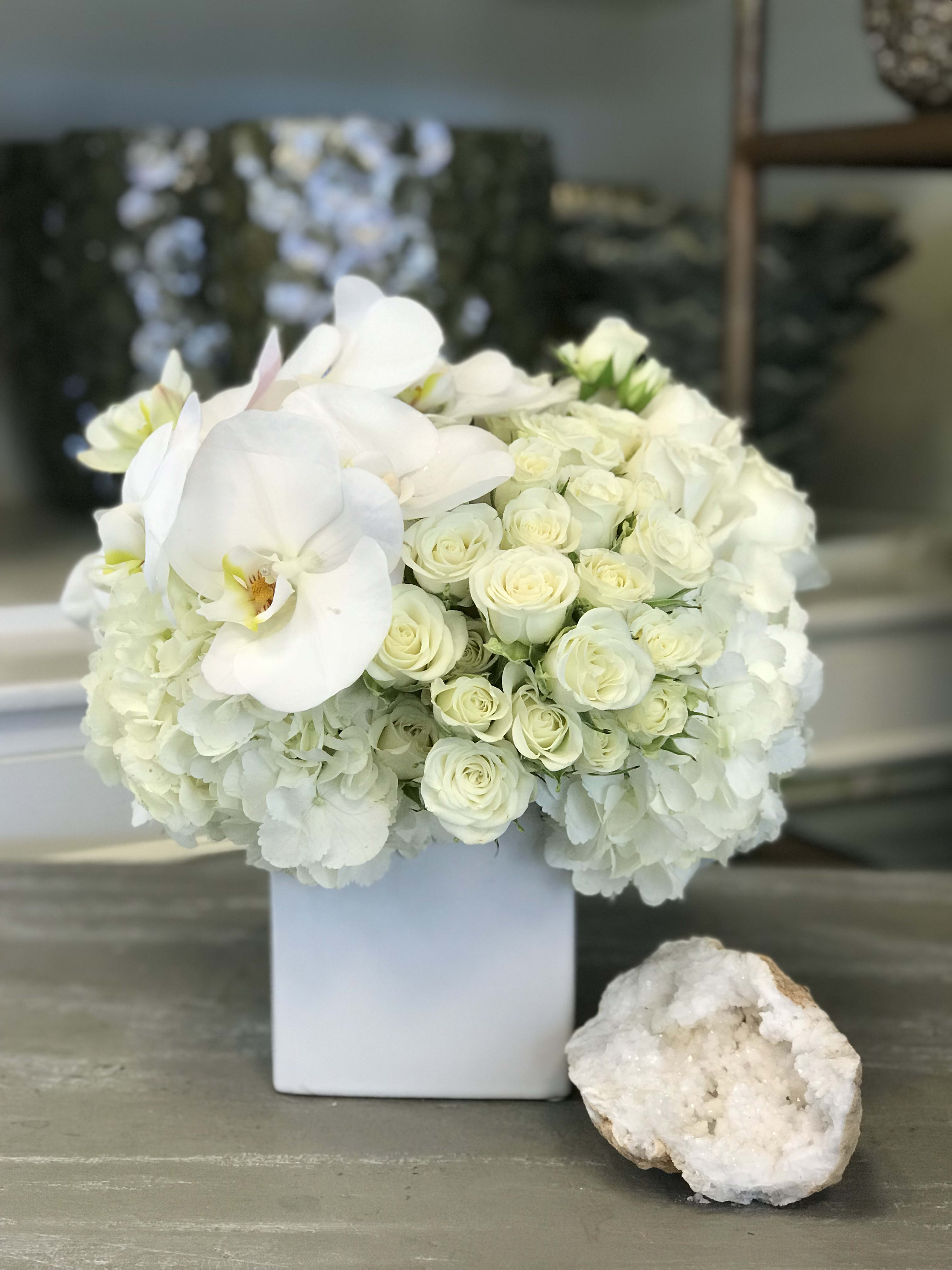 White roses and orchids arranged in a square white vase