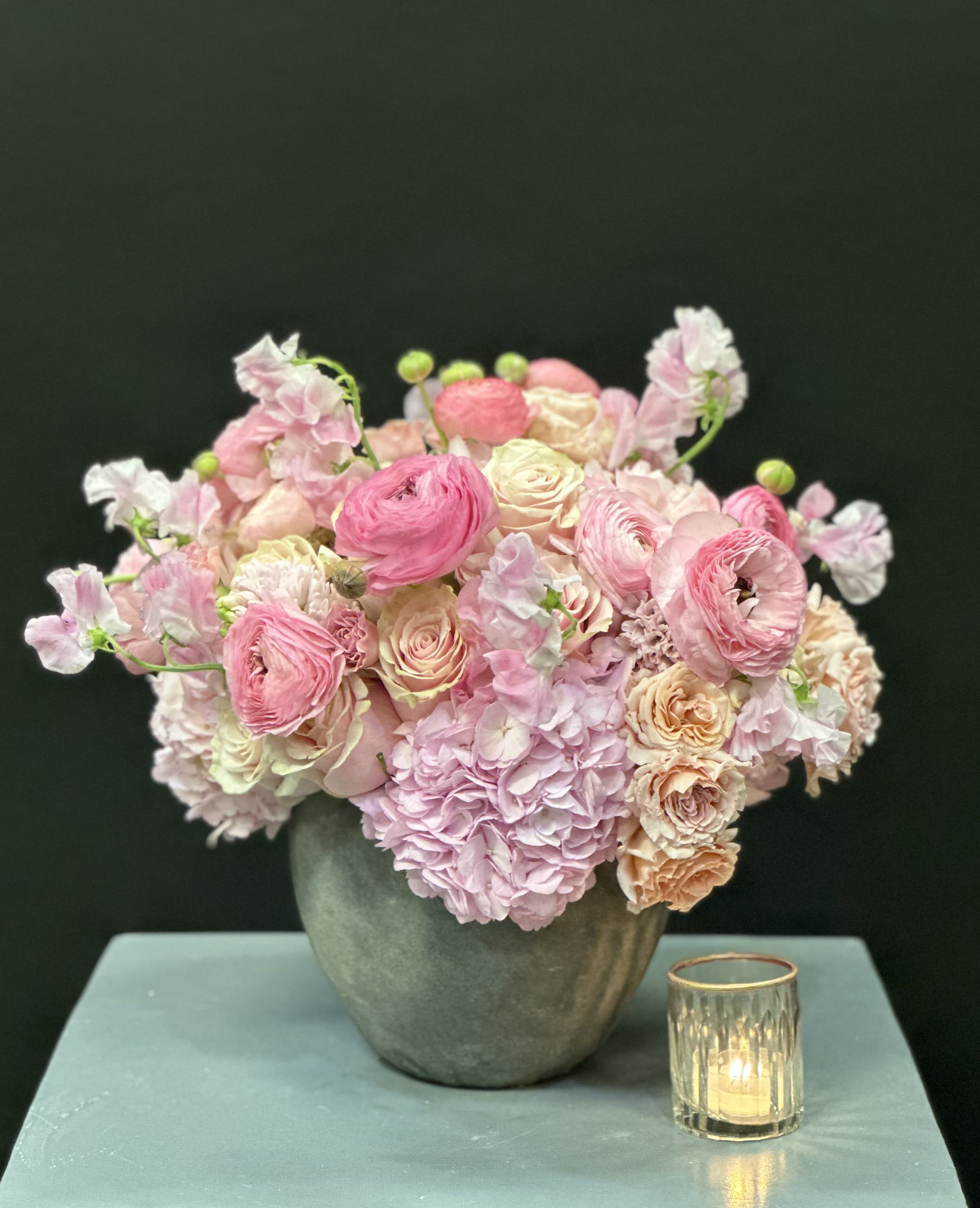 Pink and cream floral arrangement in a gray vase beside a small candle holder