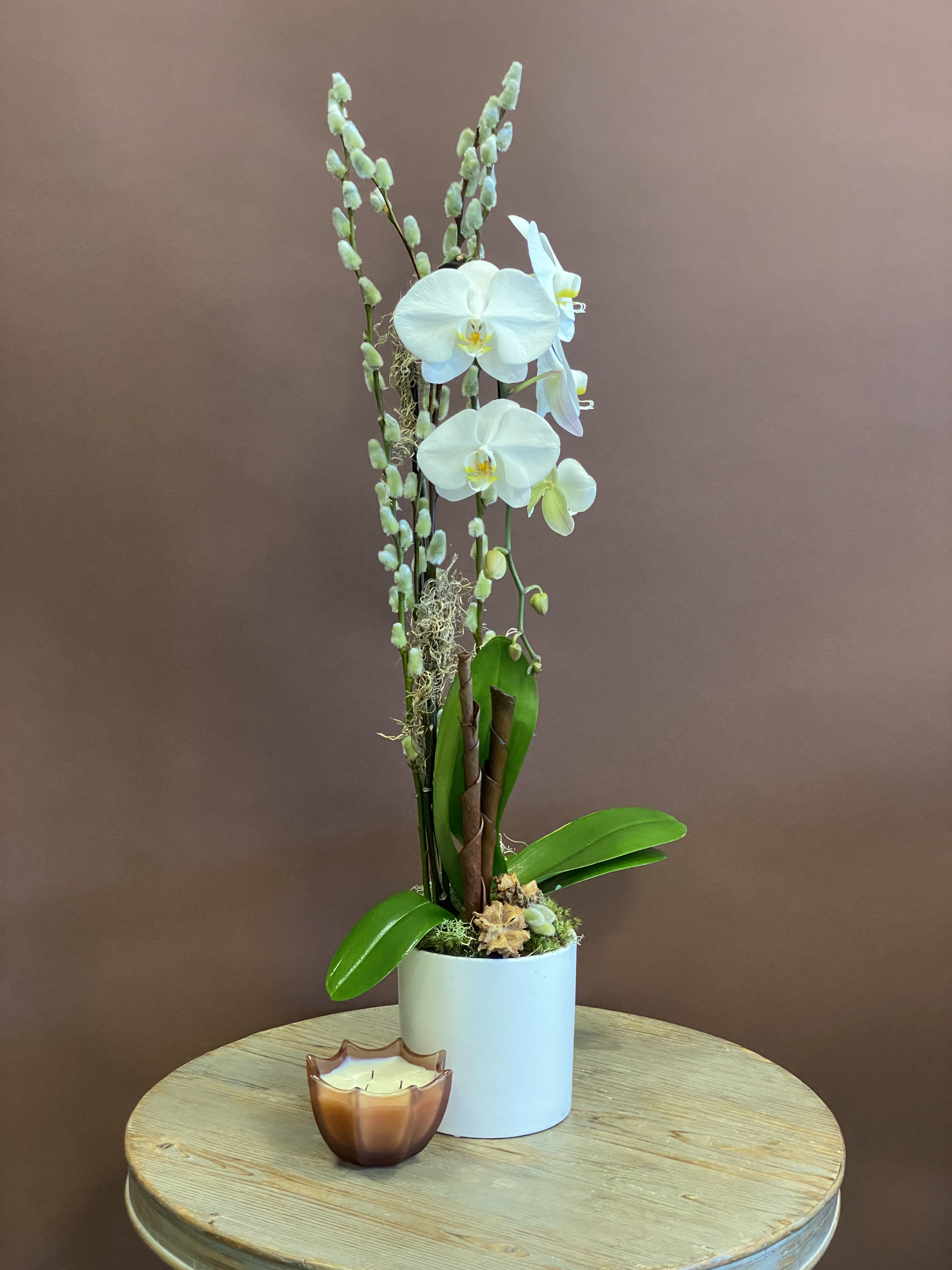 White orchid plant in a white pot with a small candle in front