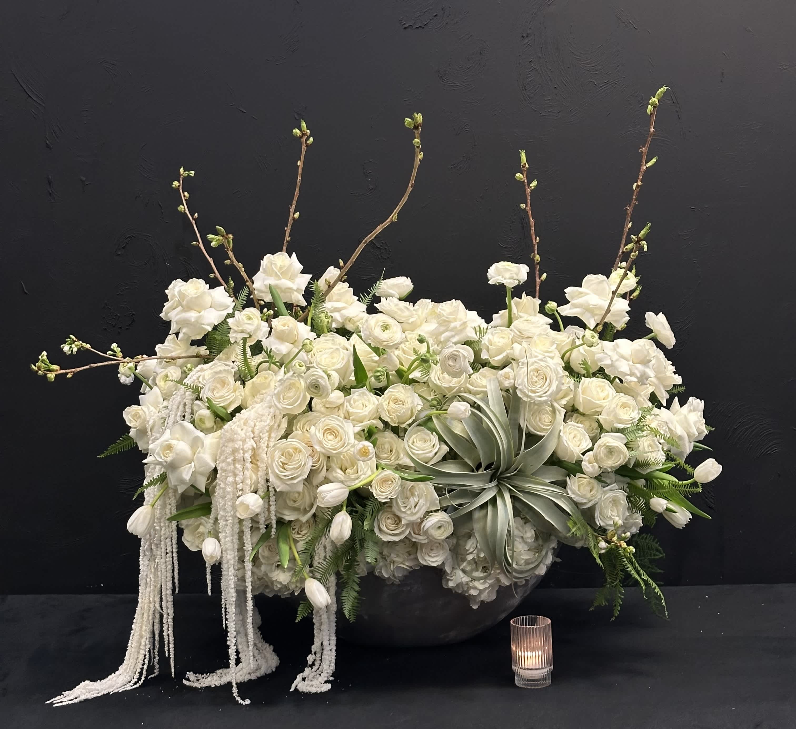 White Elegance - White Elegance boasts a captivating blend of Blossoms, White Tulips, Roses, Ranunculus  and Hydrangeas, Preserved Amaranthus and an Air Plant  creating an elegant display in a concrete oval container. The purity of the white blooms symbolizes grace and beauty.   