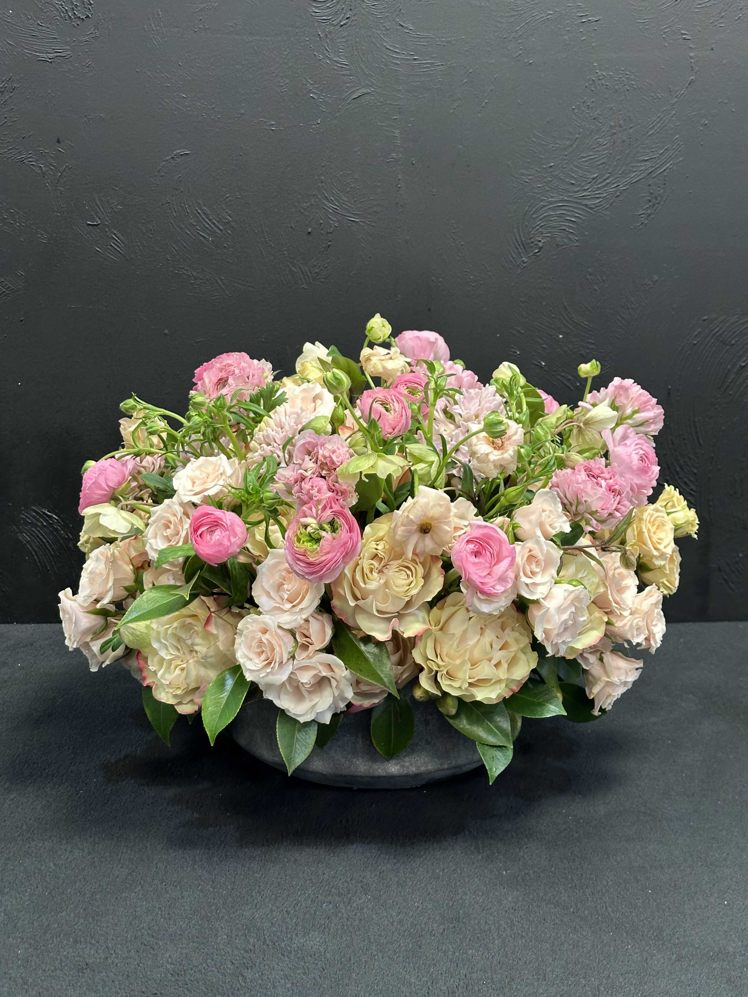 Low arrangement of pink and cream flowers in a dark bowl