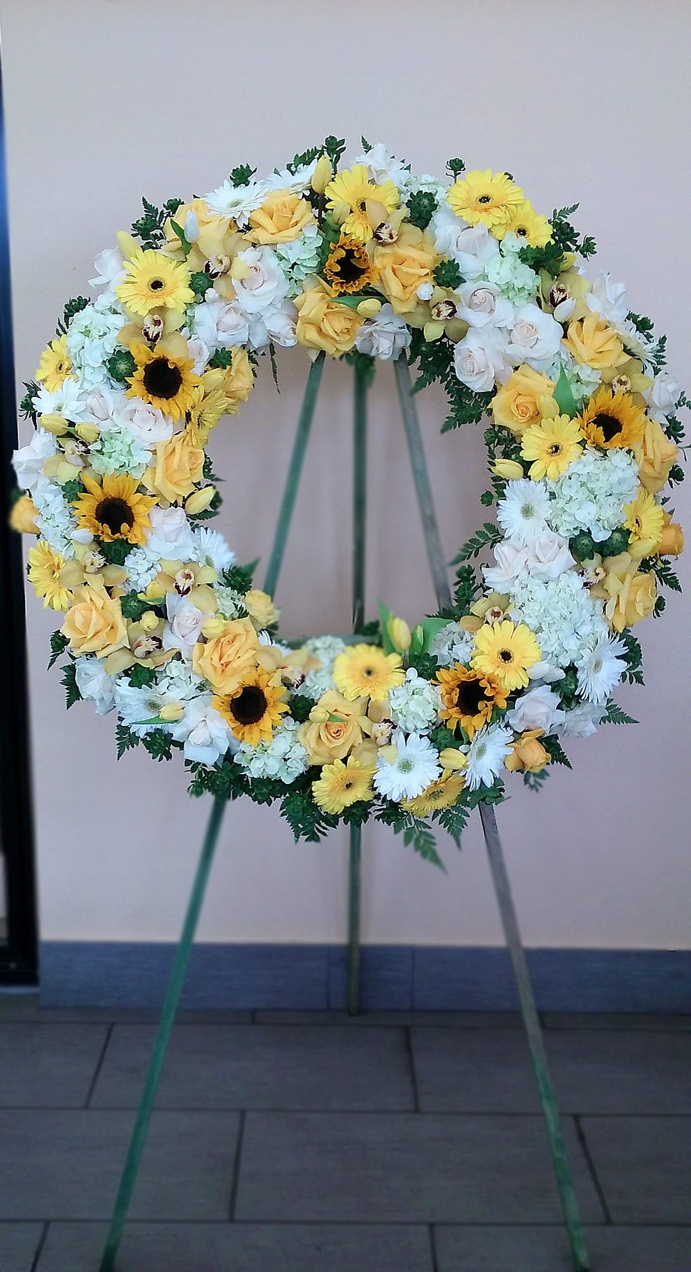 Circular floral wreath with yellow and white flowers on a stand