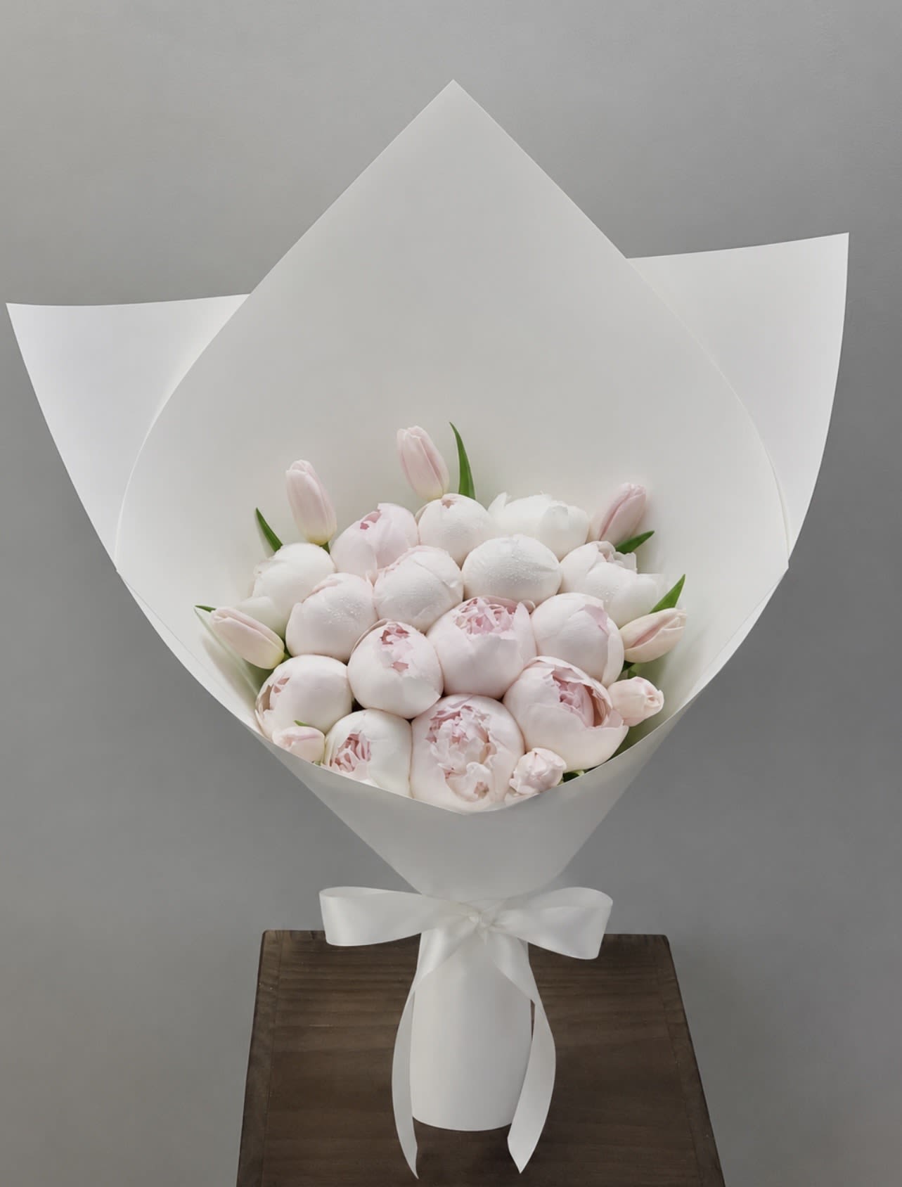 Bouquet of pale pink peonies and tulips wrapped in white paper