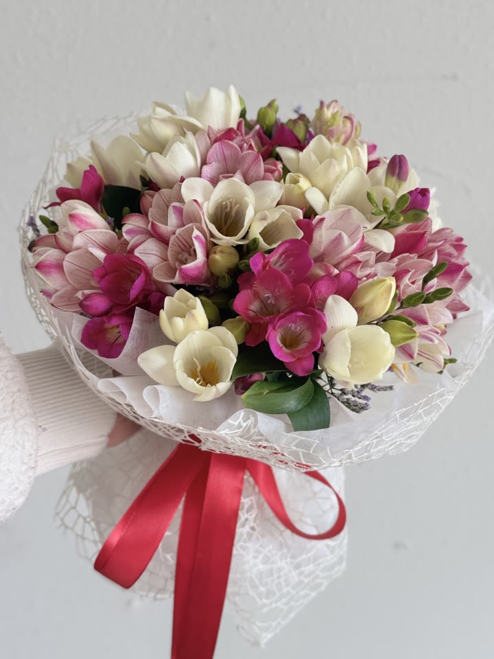 Bouquet of pink and white freesia wrapped with a red ribbon
