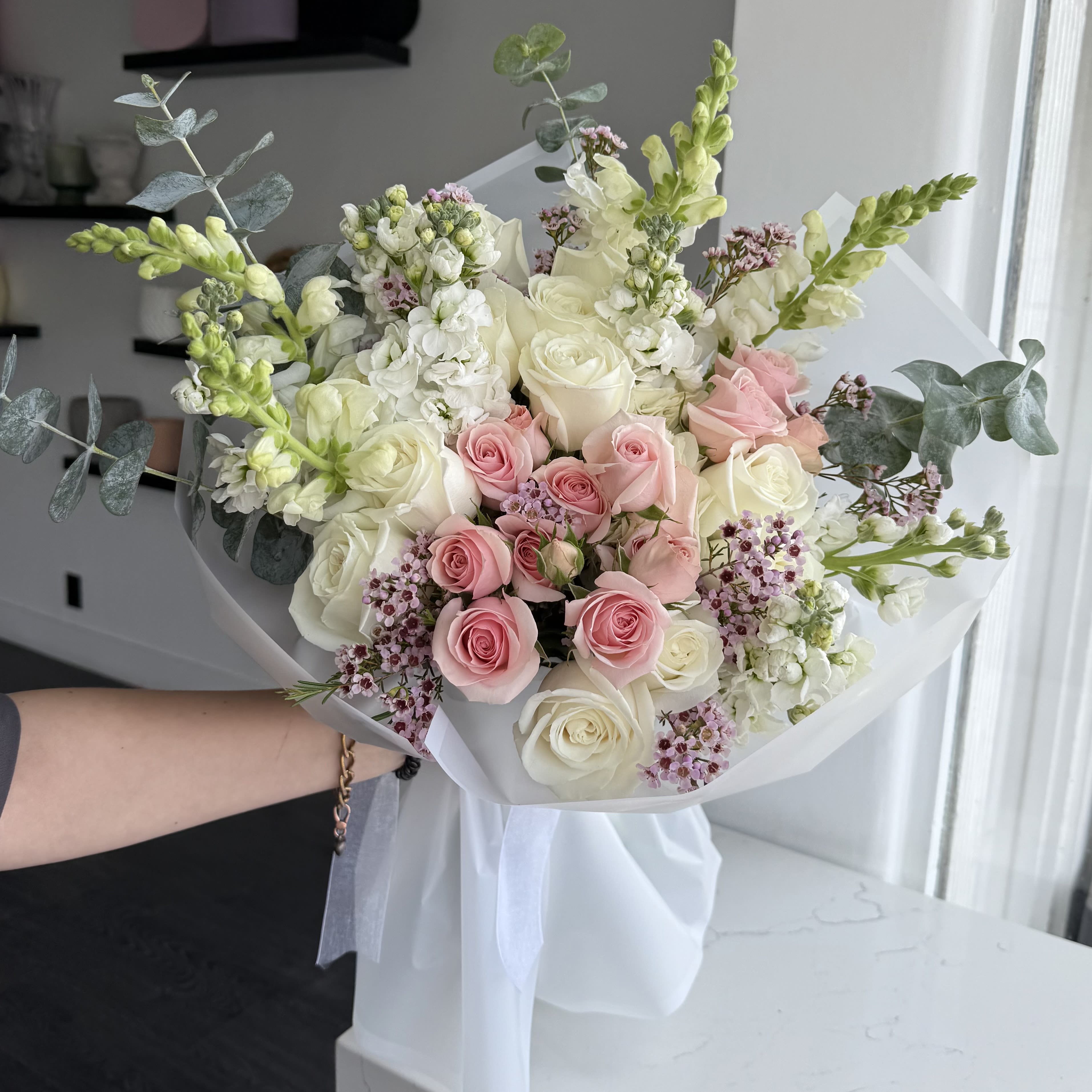 Blush Bouquet - Bouquet with pink roses, hydrangeas. Soft, romantic, and timeless — our Blush Bouquet is a delicate mix of premium roses in white and pastel pink, paired with airy seasonal fillers for a fresh, elegant look. Wrapped in white paper and finished with satin ribbon, this bouquet radiates grace and charm, making it perfect for any heartfelt occasion.   •    Premium roses in blush pink and creamy white     •    Accented with seasonal fillers for texture and volume     •    Hand-tied and wrapped in luxury paper with satin ribbon     •    Represents love, admiration, and pure elegance     •    Perfect for birthdays, anniversaries, romantic surprises, or “just because”  VASE NOT INCLUDED