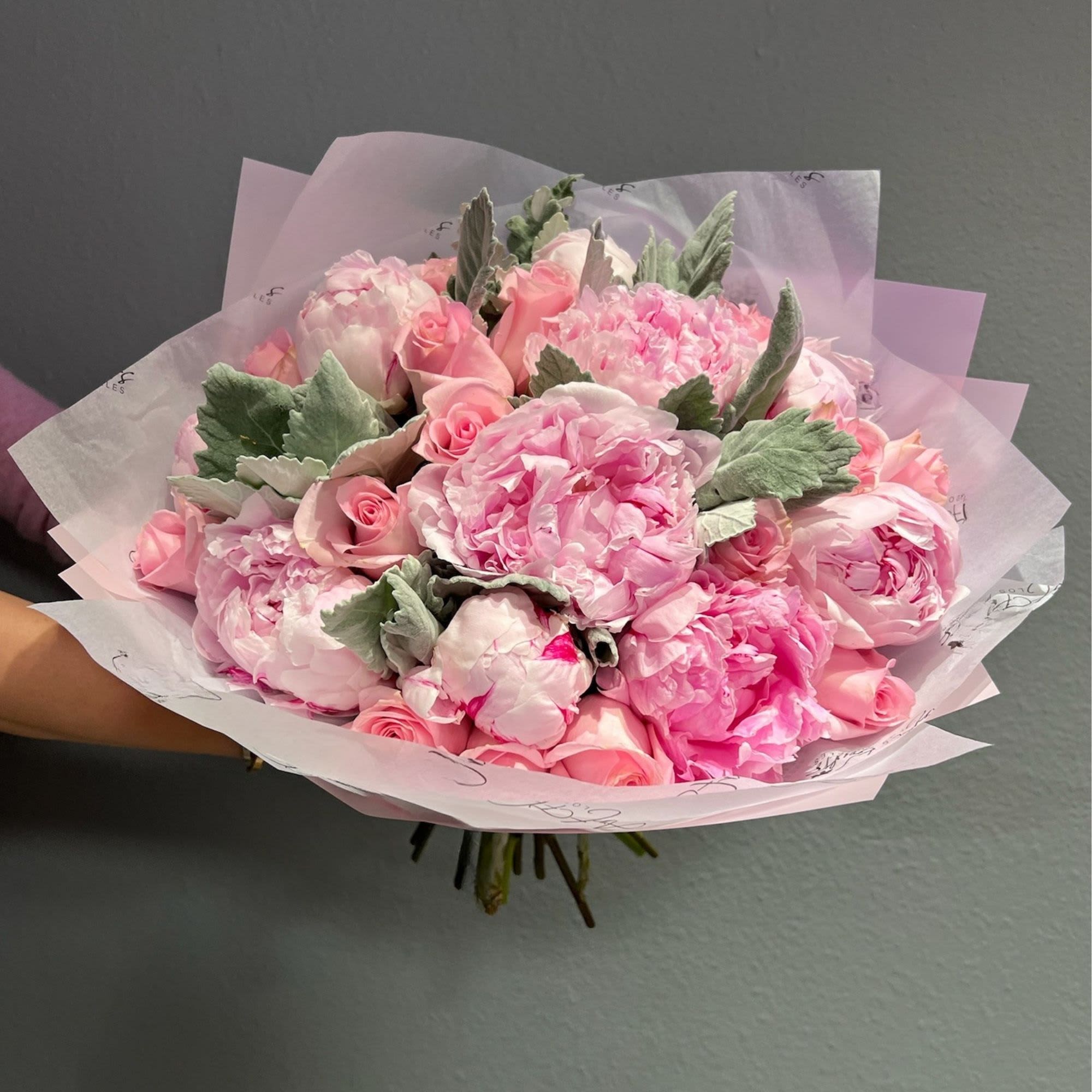 Pink bouquet of roses and peonies wrapped in pale paper