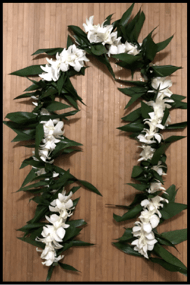 Long white flower lei with large green leaves arranged in an oval shape