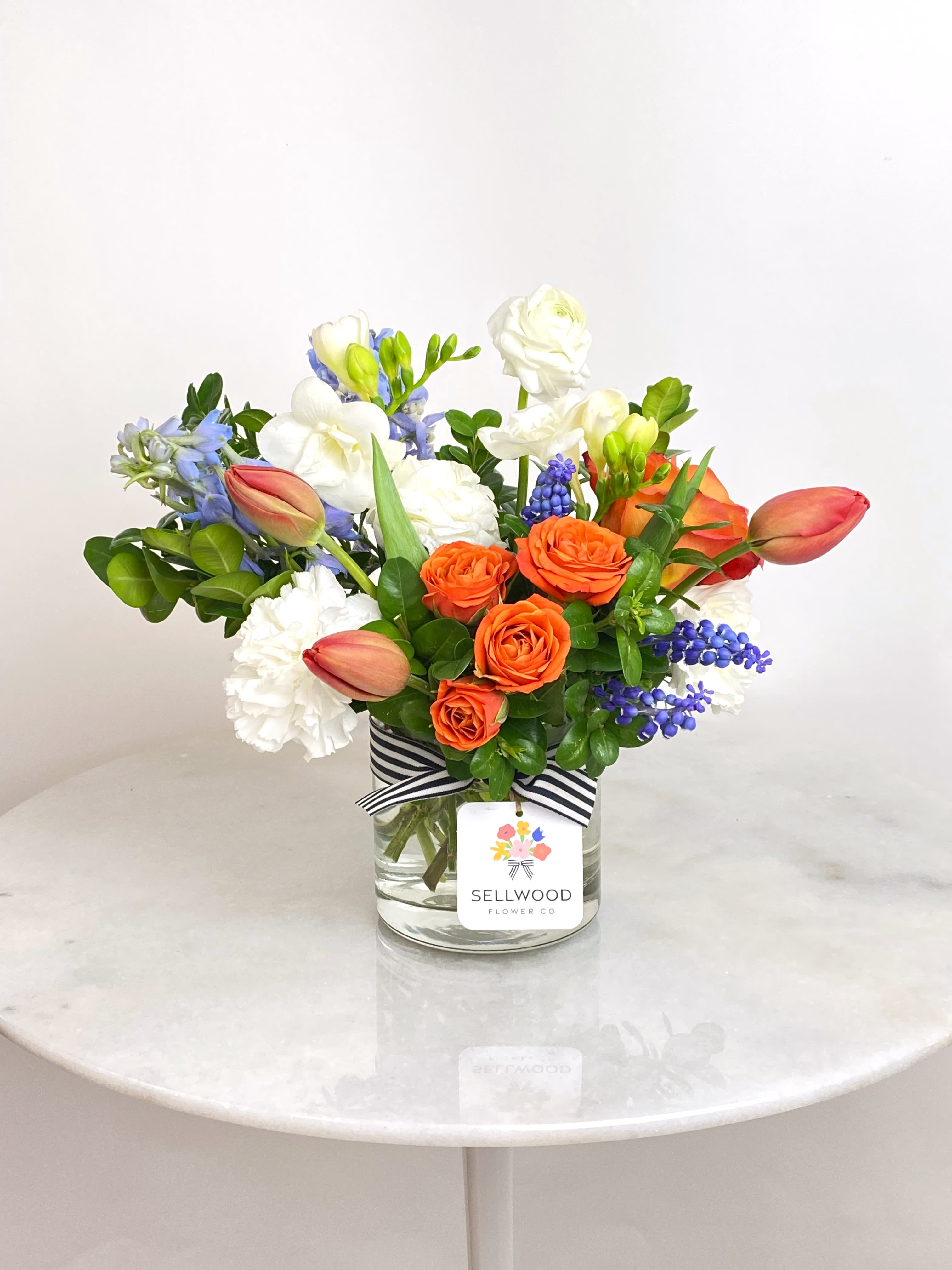 Mixed bouquet of orange and white flowers in a glass vase with a striped ribbon