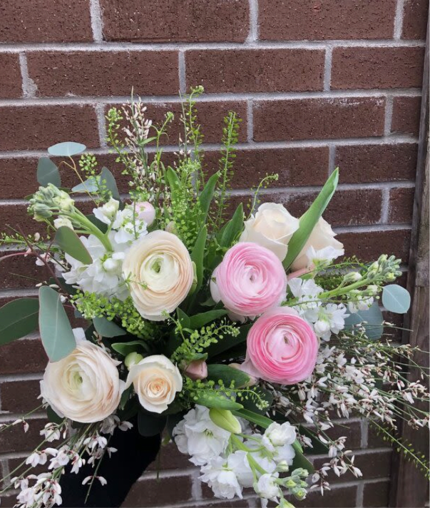 Hand-tied bouquet of pink and cream flowers with white accents.