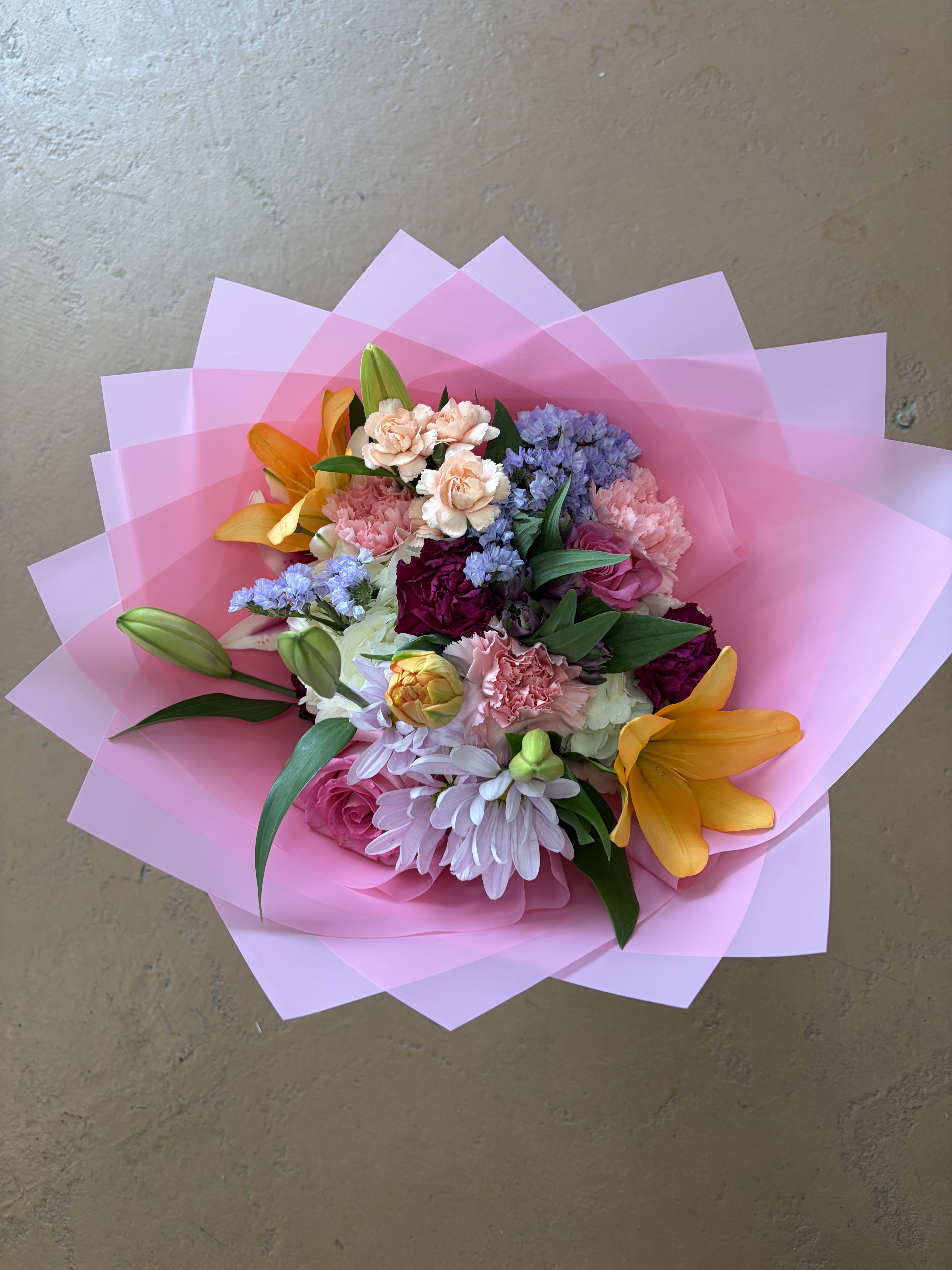 Mixed bouquet with pink, purple, and orange flowers wrapped in pink paper
