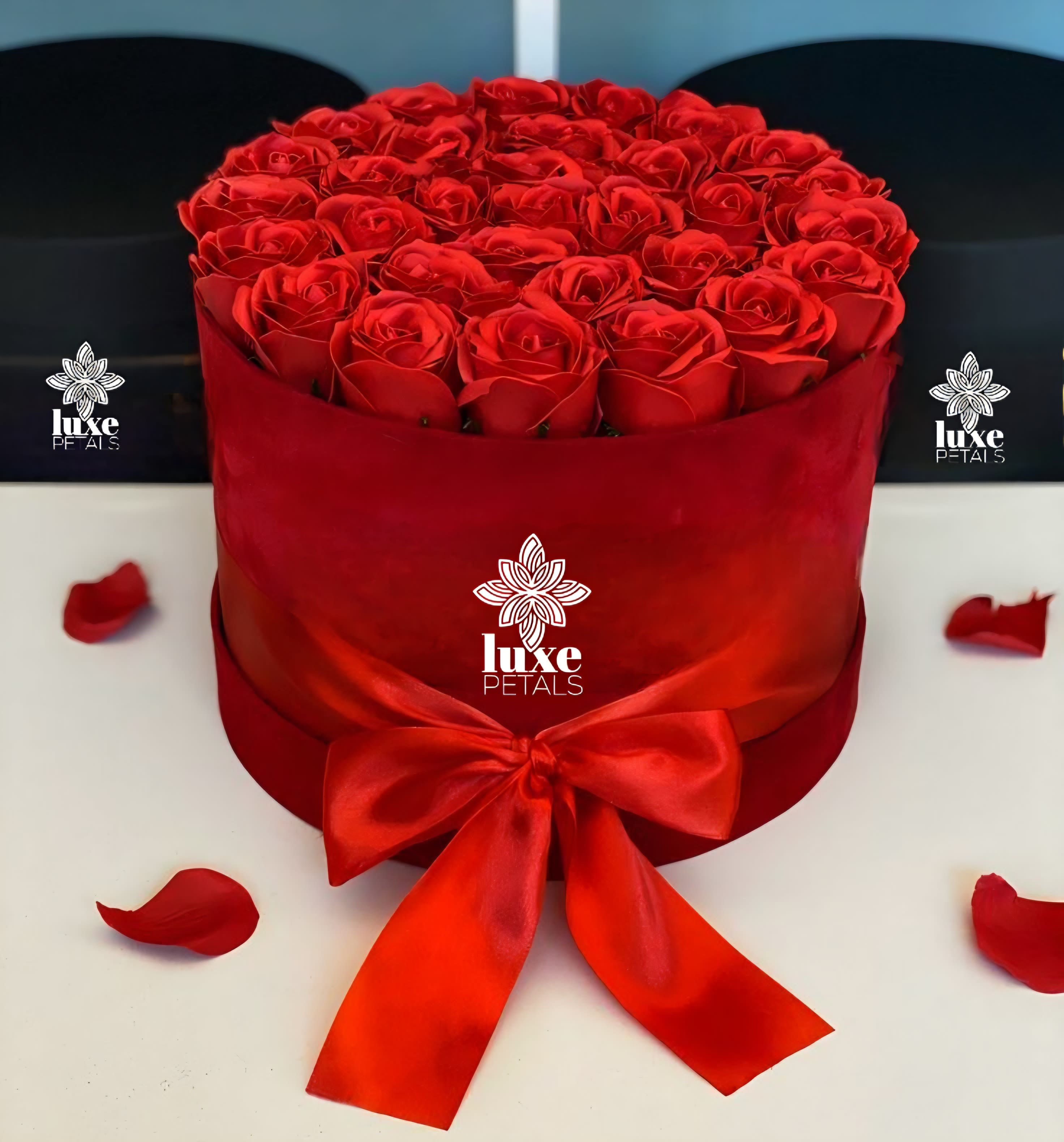 Circle Love - A dense dome of velvety red roses crowns a round red hat box, an instantly romantic flower arrangement perfect for anniversaries, Valentine's Day, or saying "I love you" just because. The monochromatic red palette and sculpted, uniform silhouette create a modern, upscale look that will make the person you're thinking of feel deeply cherished-equally fitting for birthdays, Mother's Day, or a dramatic centerpiece at a holiday table.  Each arrangement features tightly clustered long-stem roses set low in the box to form a seamless, luxurious top; the box itself is wrapped in rich red material and finished with a wide red satin ribbon bow for a polished, gift-ready presentation. A few loose petals around the base add a softly romantic, tactile detail. The compact, wearable size makes it easy to display on a bedside table, office desk, or dining room centerpiece.  This elegant presentation sends clear emotion-love, appreciation, or a heartfelt apology-without saying a word, making it an excellent choice for occasions from Thanksgiving and Christmas to graduations, get-well wishes, and weddings. Order with confidence for same-week gifting; keep flowers in a cool spot away from direct sun and refresh the water if provided to help blooms stay vibrant longer.