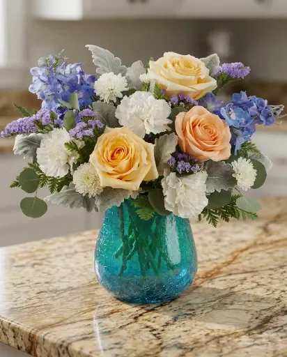Coastal Pastel Serenity - Soft, elegant, and effortlessly calming, Coastal Pastel Serenity features creamy peach roses, delicate blue hydrangeas, white carnations, lavender statice, and textured silver foliage arranged in a vibrant turquoise glass vase. This airy garden-style arrangement brings together soothing coastal tones with a fresh floral touch, making it perfect for birthdays, sympathy gestures, thank you gifts, or simply brightening someone’s day.