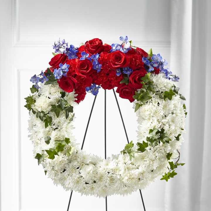 Patriotic Passion Wreath - Our Patriotic Passion Wreath is a beautiful symbol of honor, bravery and loyalty. Each arrangement is handcrafted with a collection of cushion pompons, roses and delphinium to create the tribute they deserve for their sacrifice. 