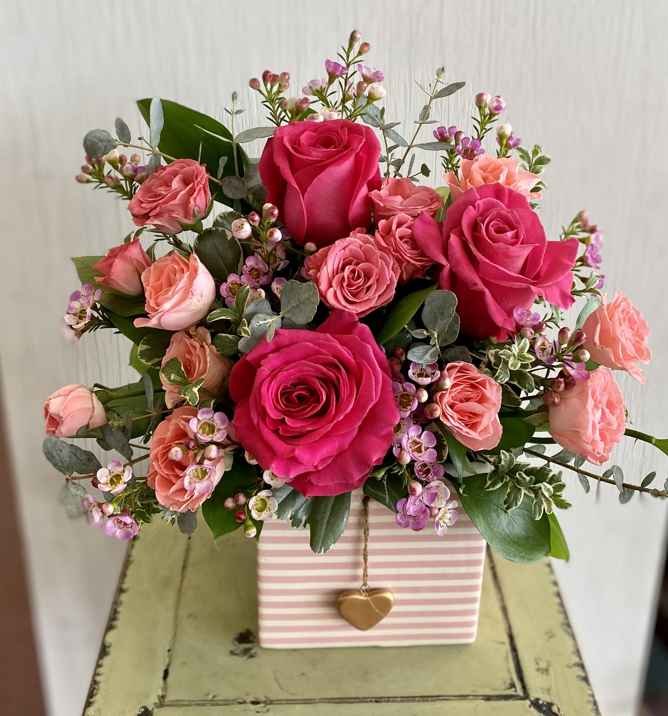 Pink and coral rose bouquet in a striped gift box with a heart charm