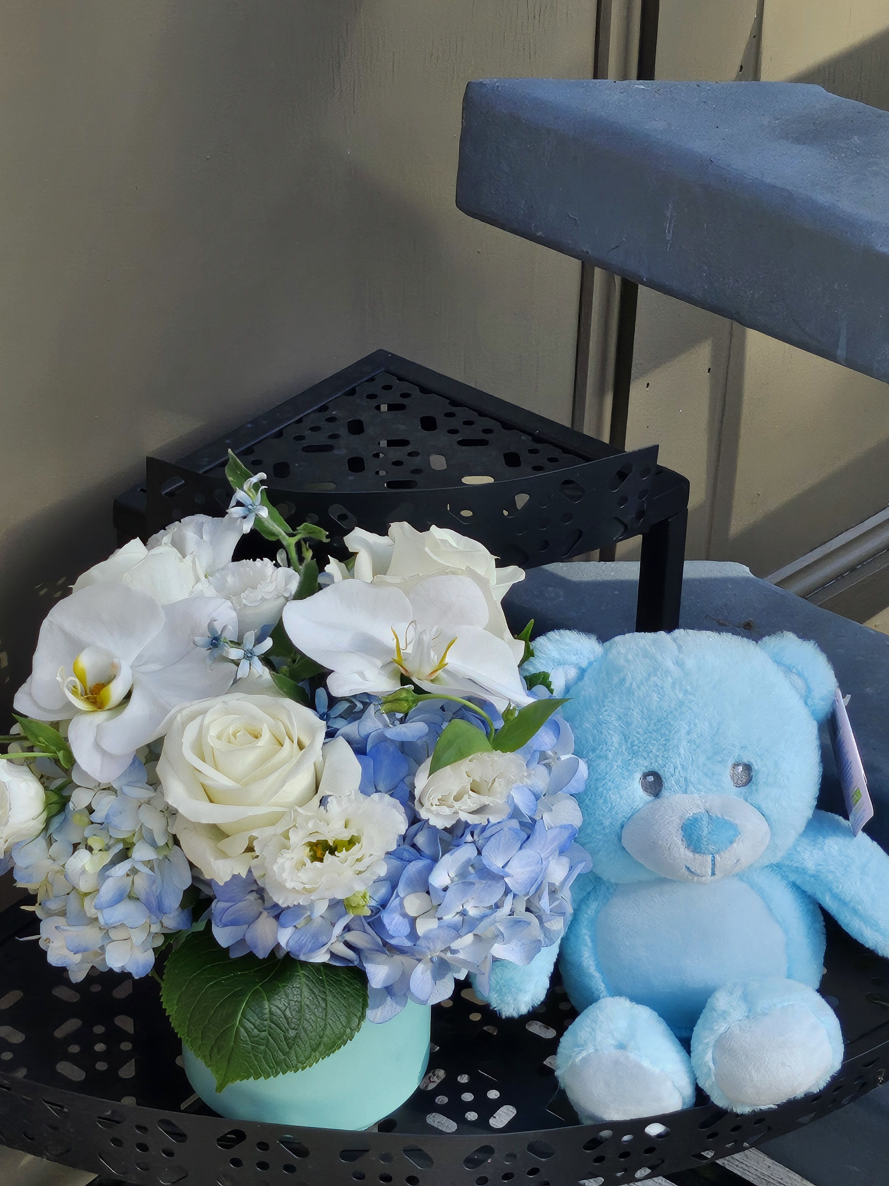 White and blue flower arrangement beside a light blue teddy bear